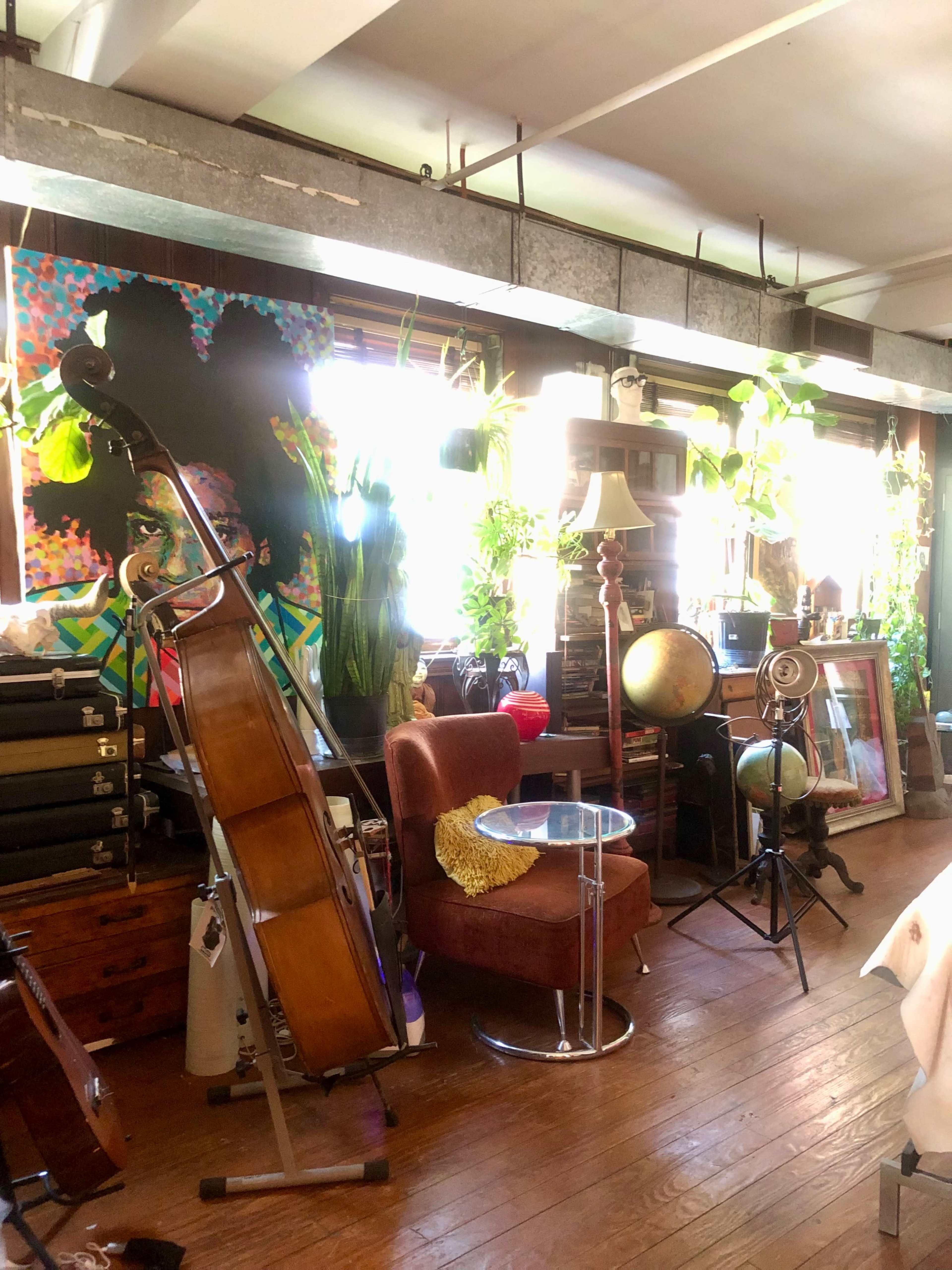 A cluttered room filled with plants, a cello, a brown chair, a globe, and various pieces of furniture and decor.
