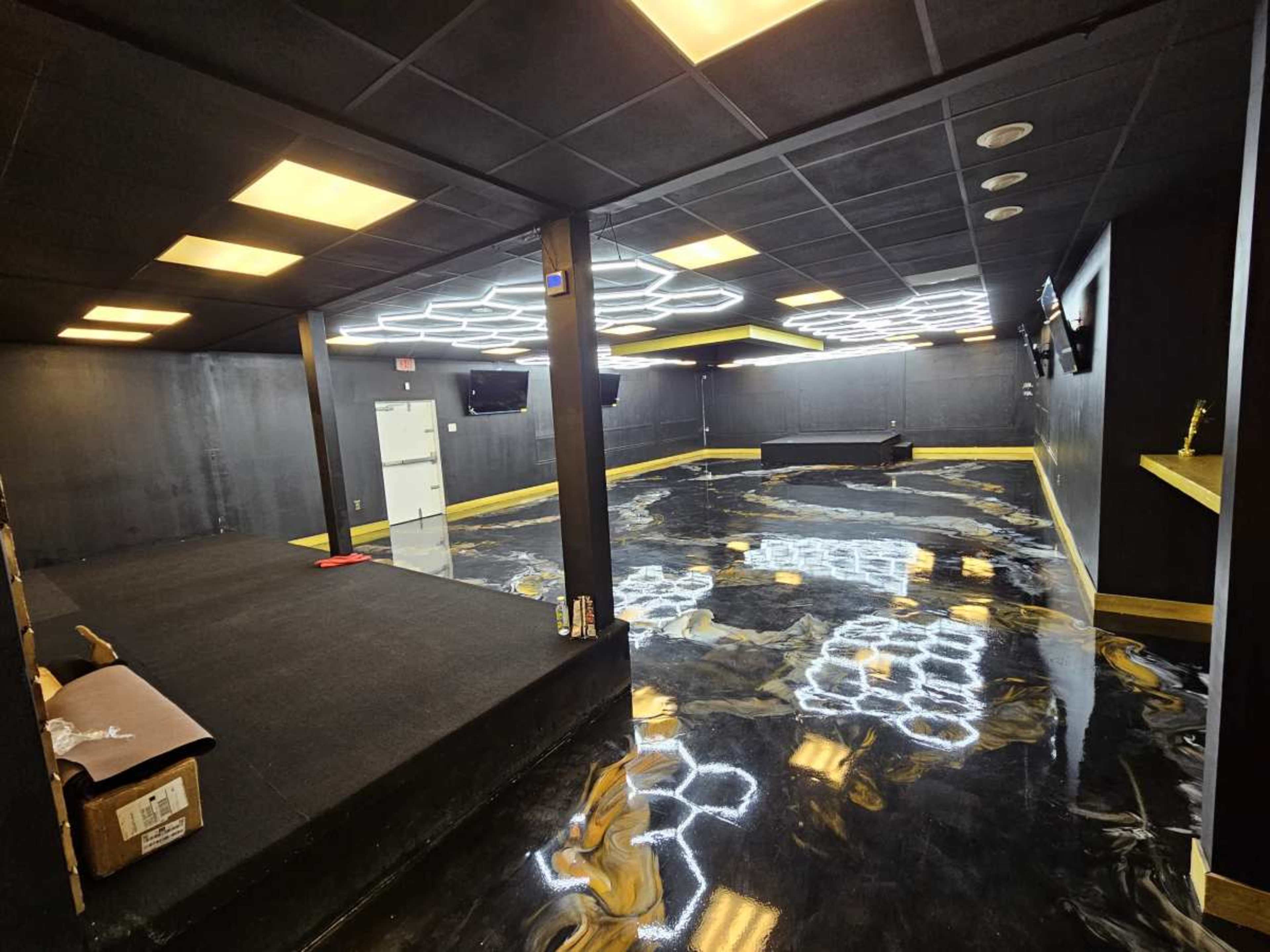 The image shows an empty modern studio space with a black floor, yellow accents, and illuminated geometric light fixtures on the ceiling.