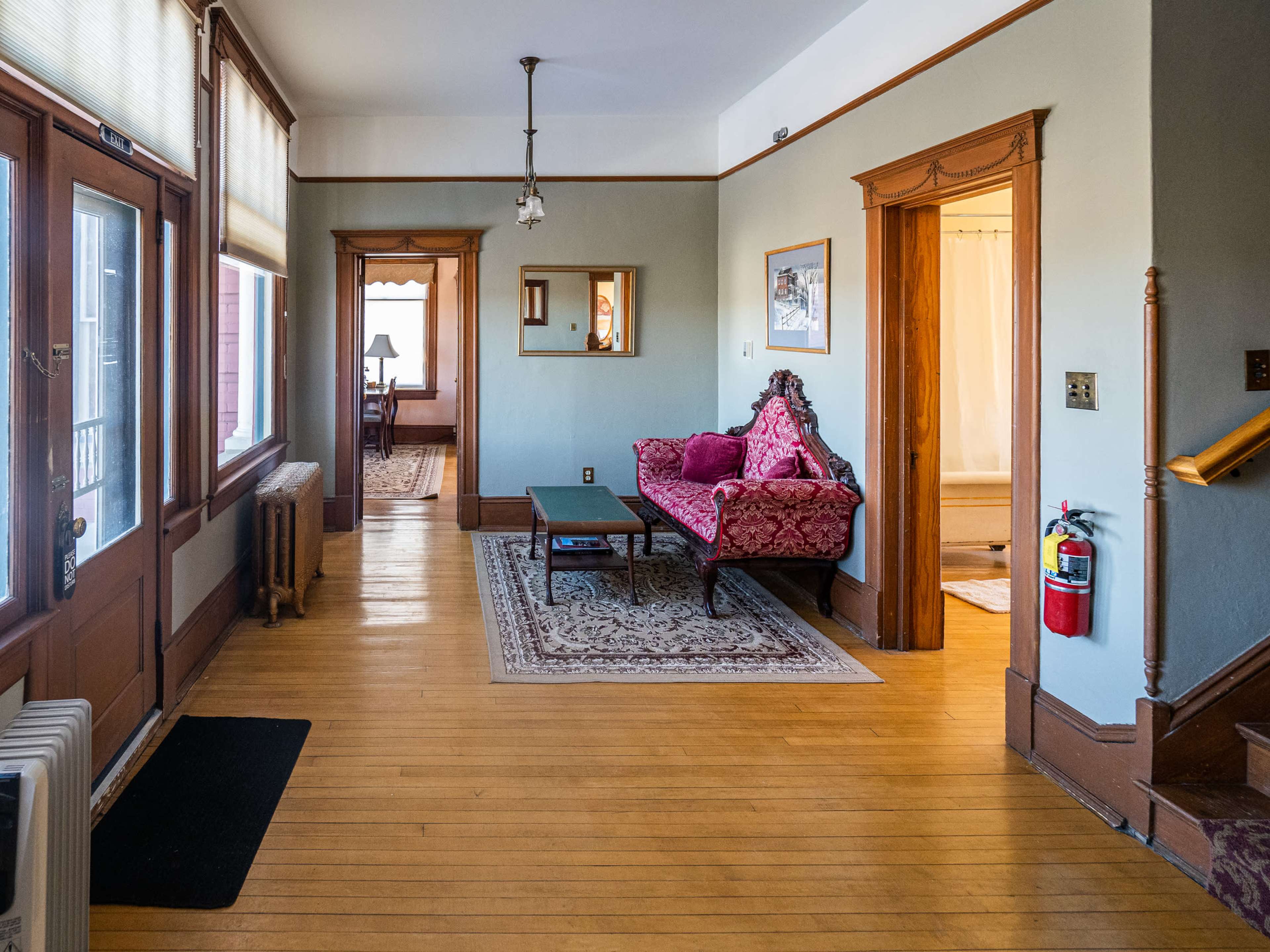 The image shows a partially furnished hallway with a red patterned couch, a coffee table, and doorways leading to other rooms.