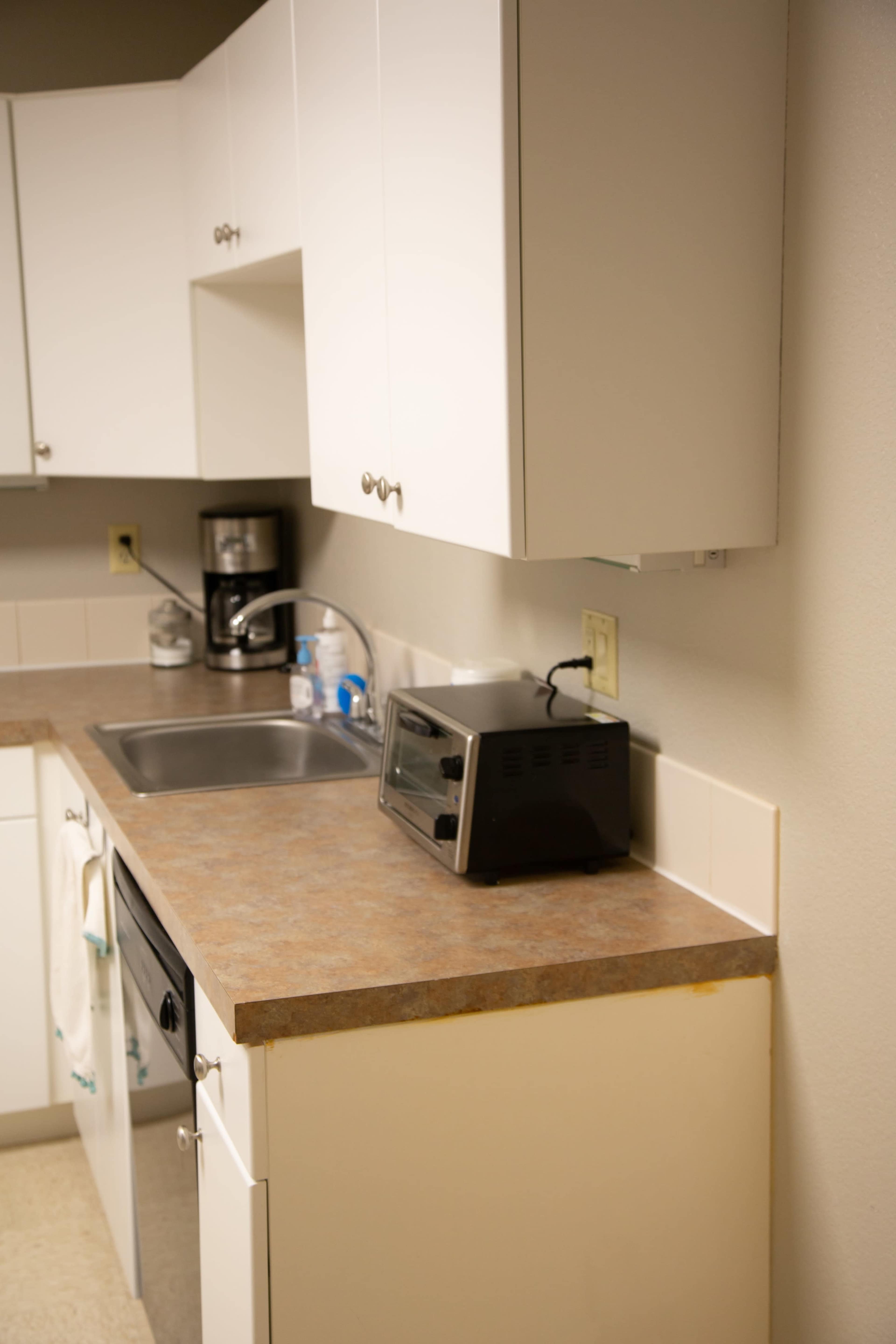A kitchen countertop with a sink, a toaster, and a coffee maker on the shelves above.