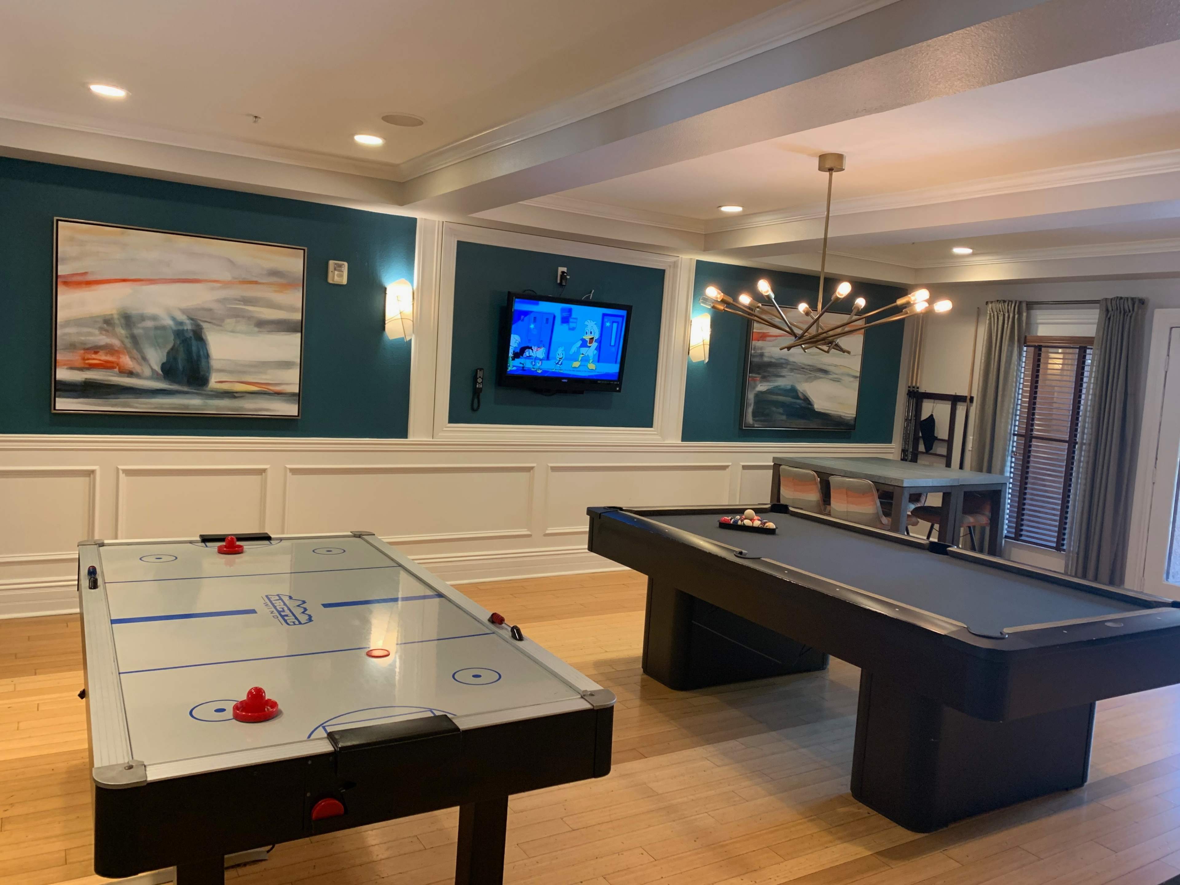 A recreational room featuring an air hockey table, a pool table, and a television mounted on the wall.