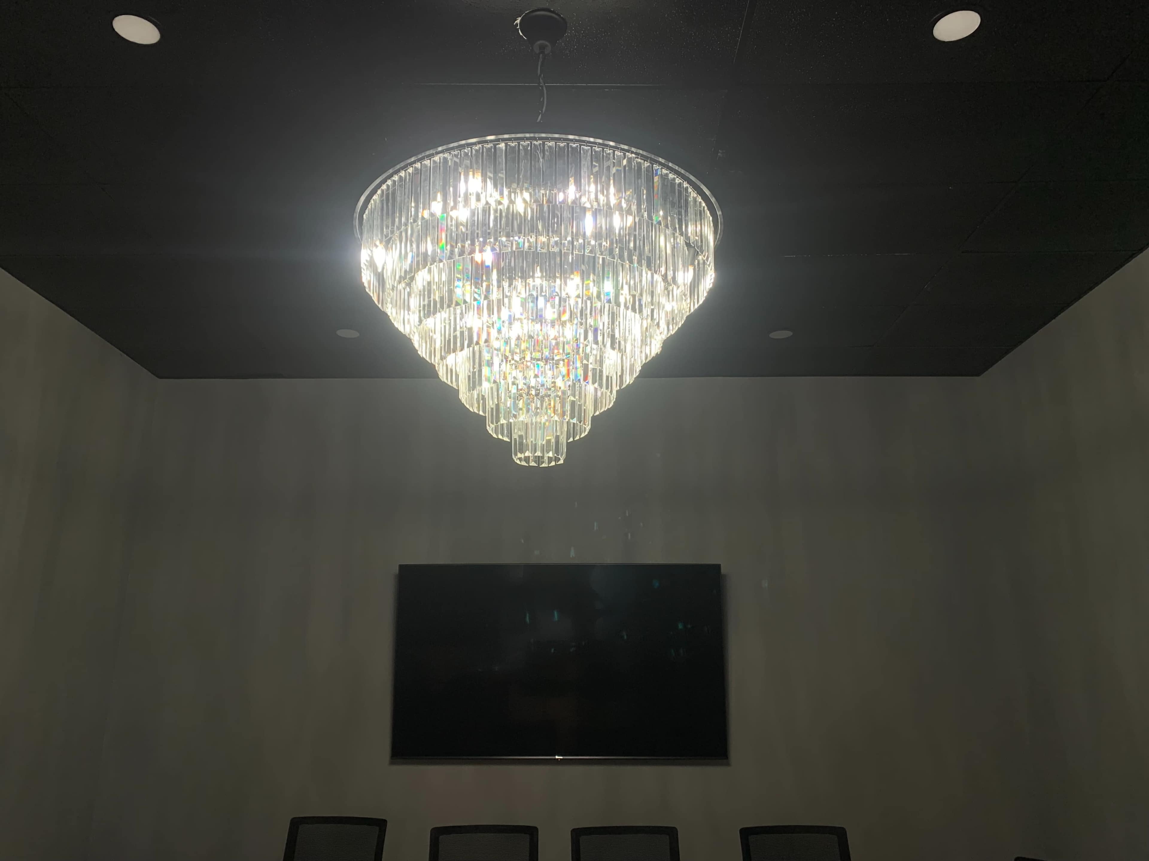 A large crystal chandelier hangs from the ceiling above a dark conference room with a blank screen on the wall.