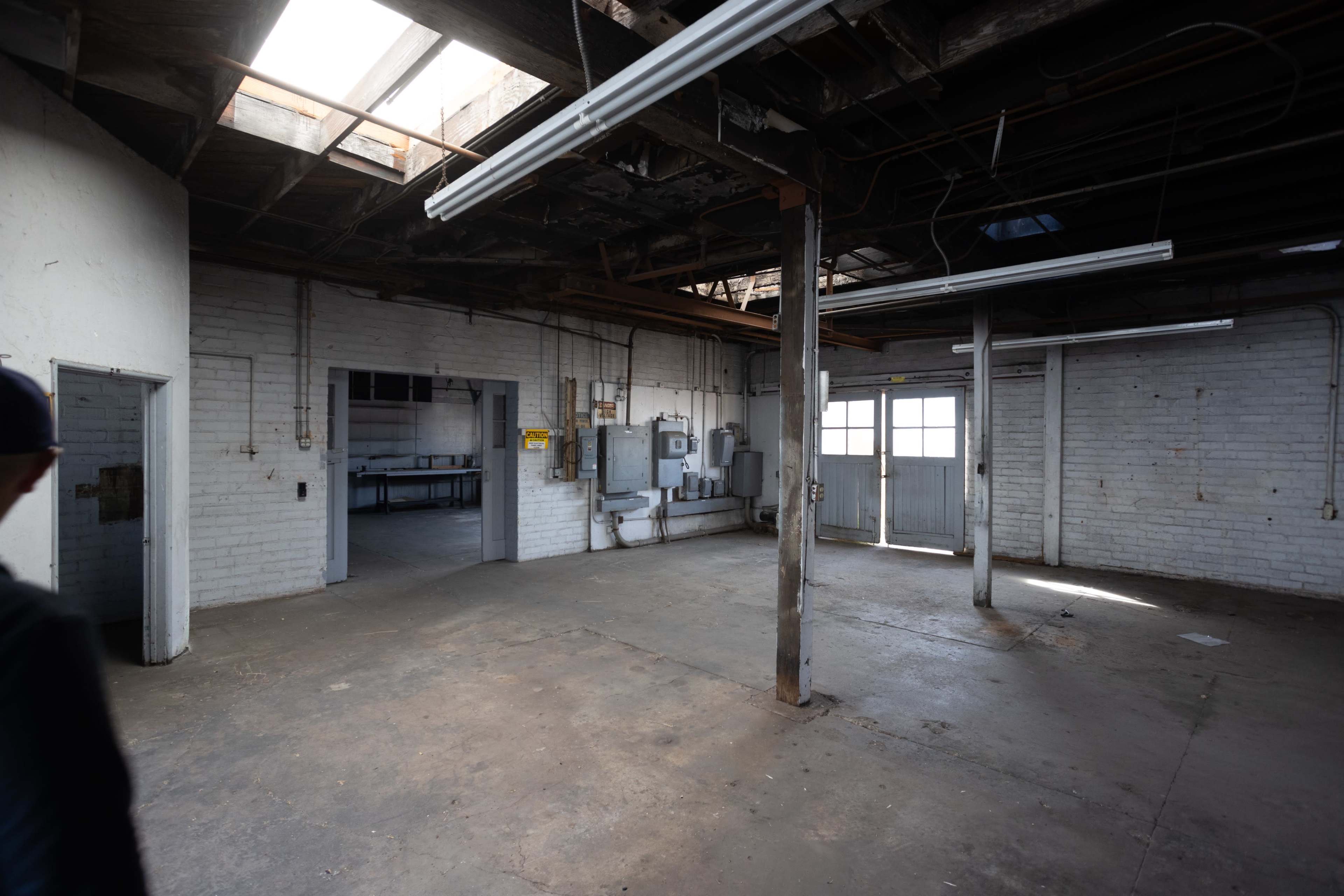An empty industrial space with exposed beams, concrete flooring, and two entrances.