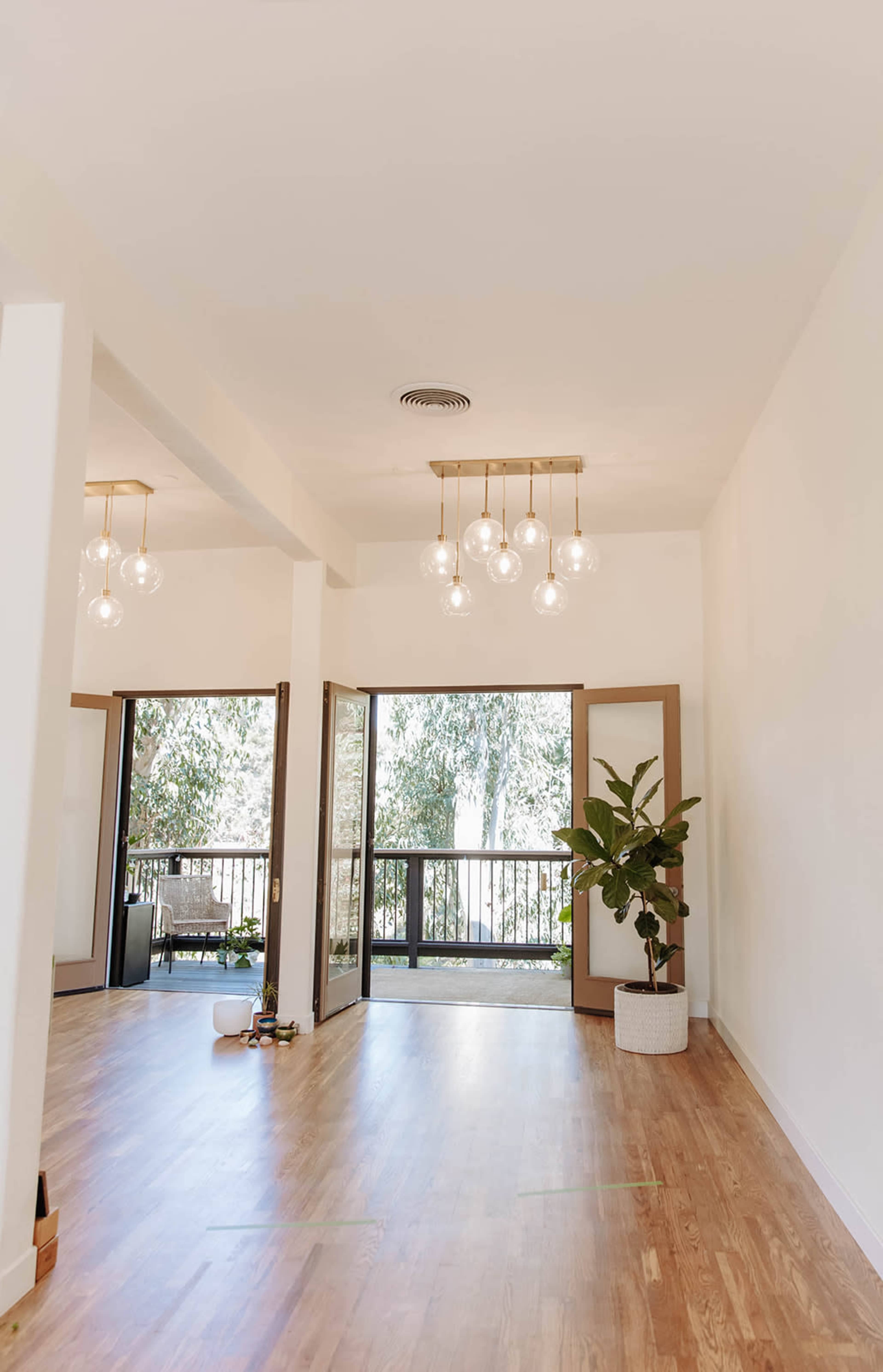 The image shows a wooden-floored interior space with large windows, a potted plant, and modern pendant lighting.