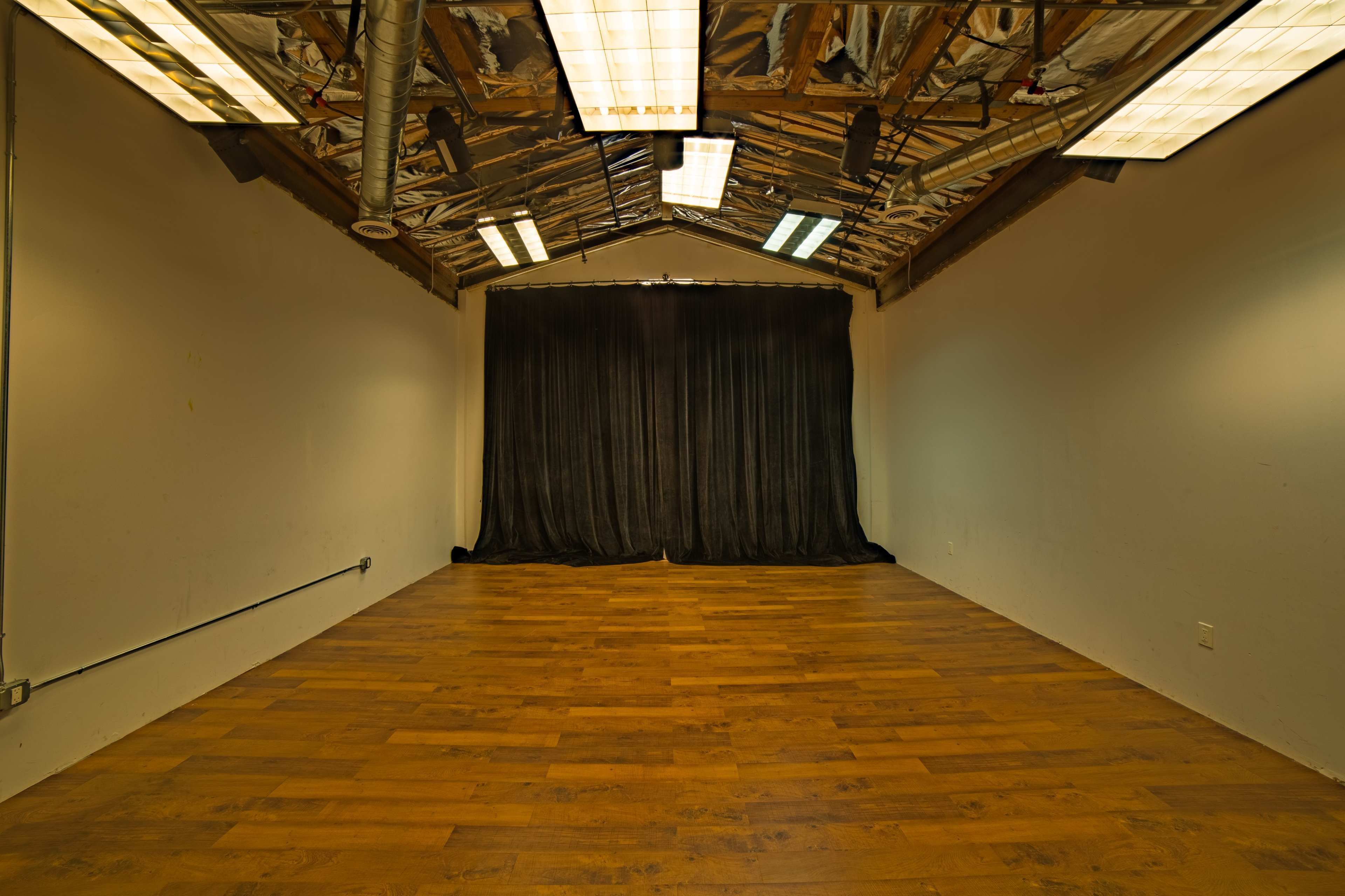 An empty room with wooden flooring, exposed beams, and a black curtain at one end.