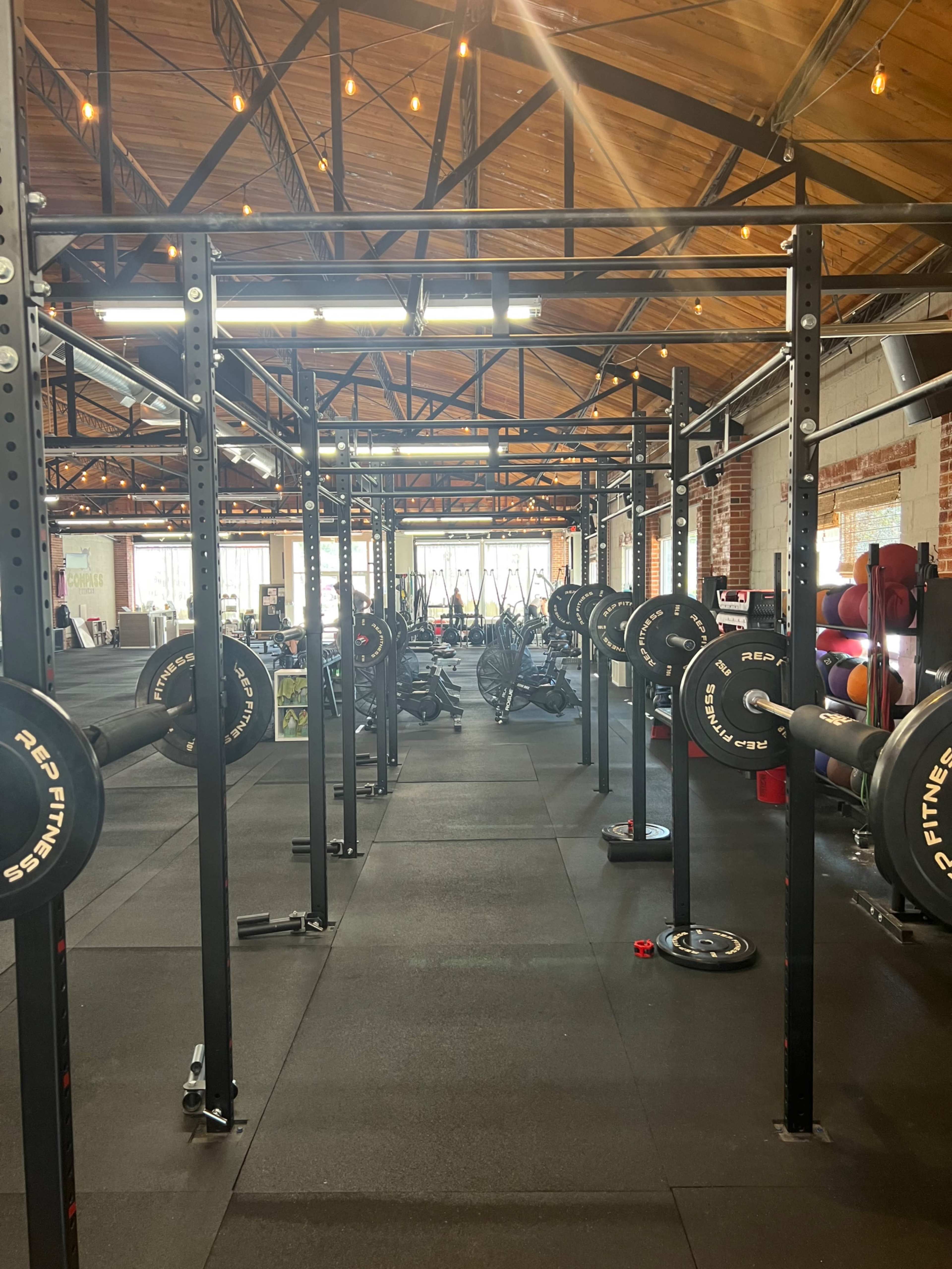 The image shows an industrial-style gym with weightlifting equipment arranged in neat rows and a textured flooring surface.
