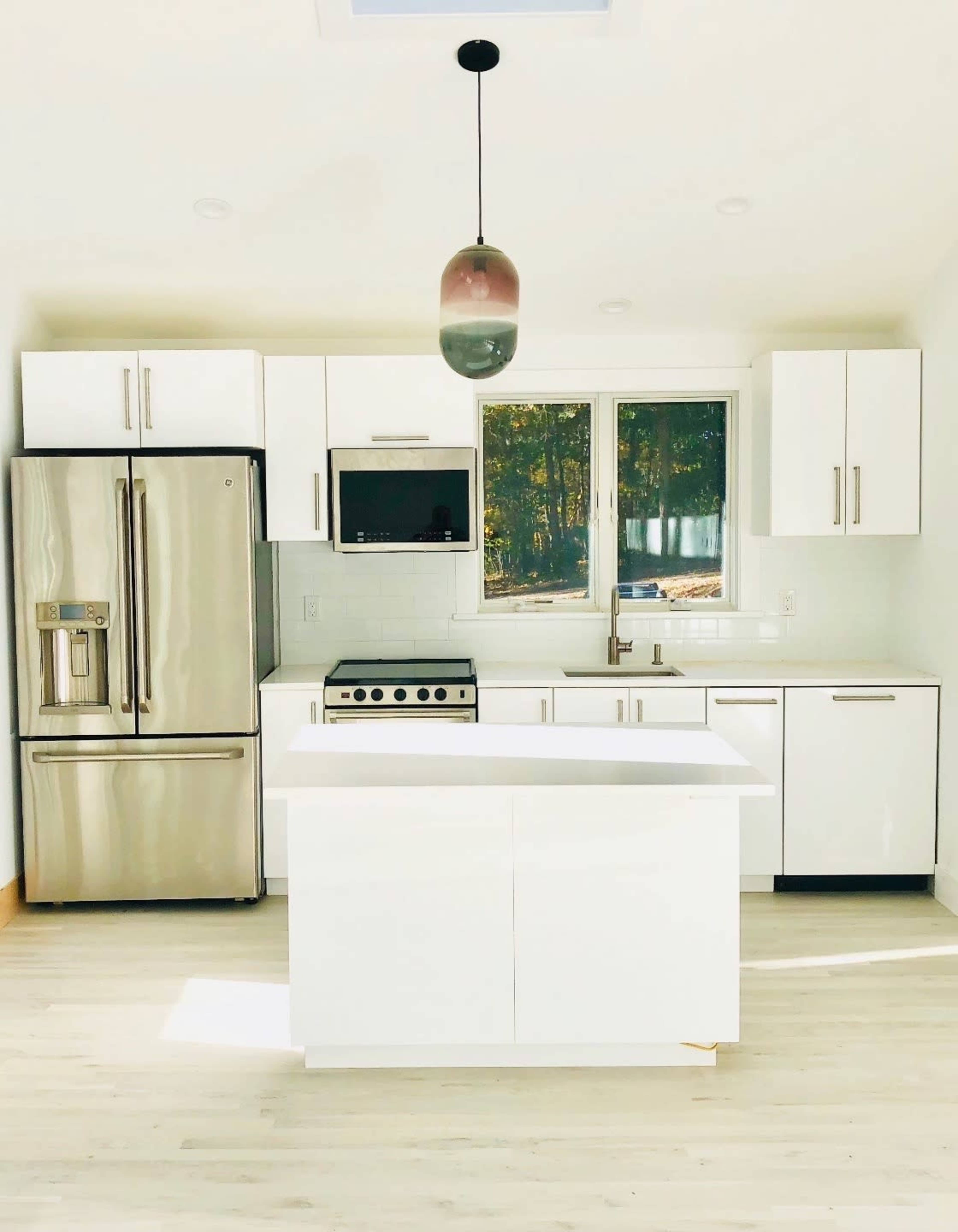 The image shows a modern kitchen with white cabinets, stainless steel appliances, and a central island beneath a pendant light.