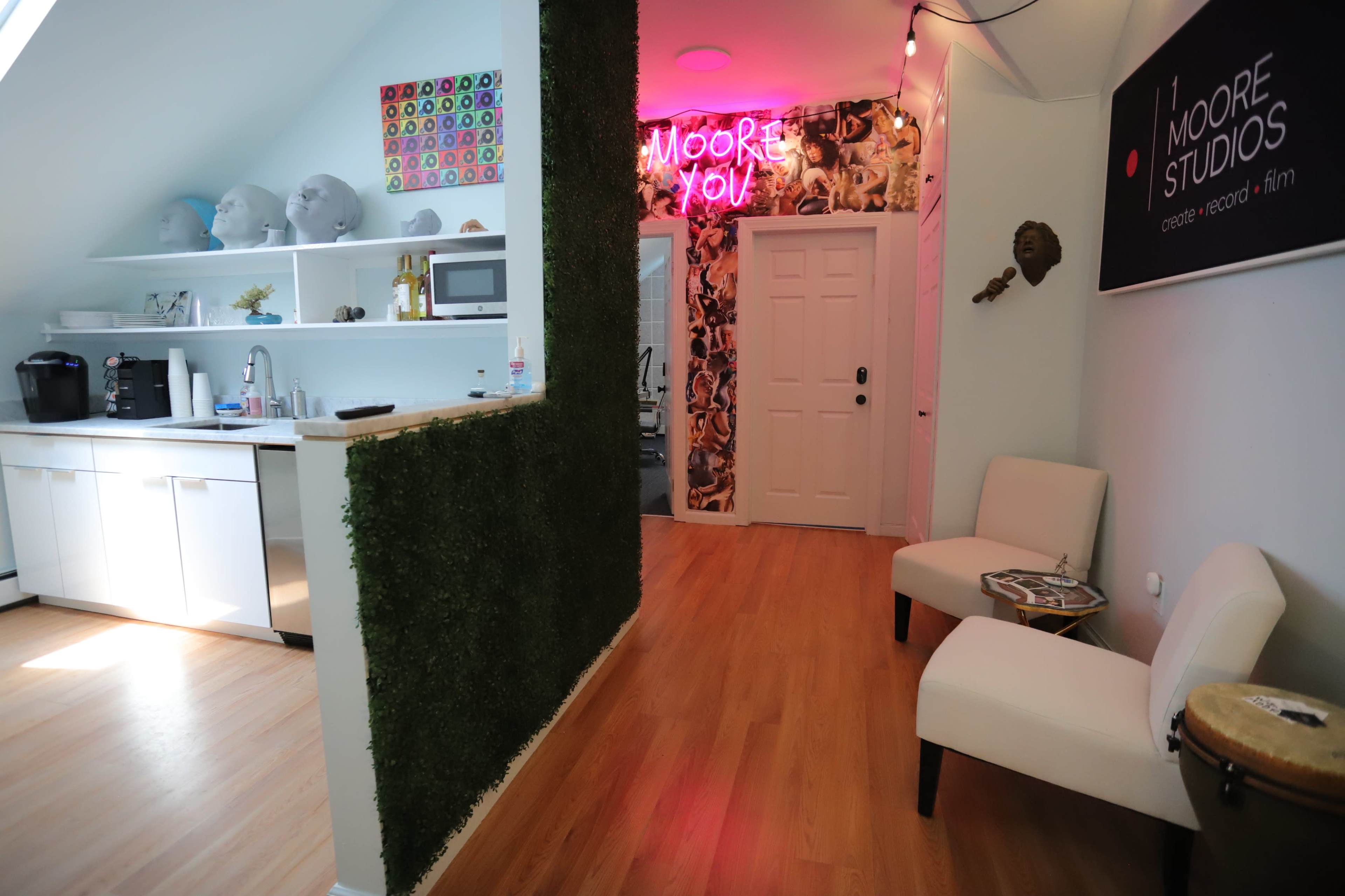 A modern studio interior with a kitchenette on one side, a decorative green wall, and a seating area with two chairs in a well-lit space.