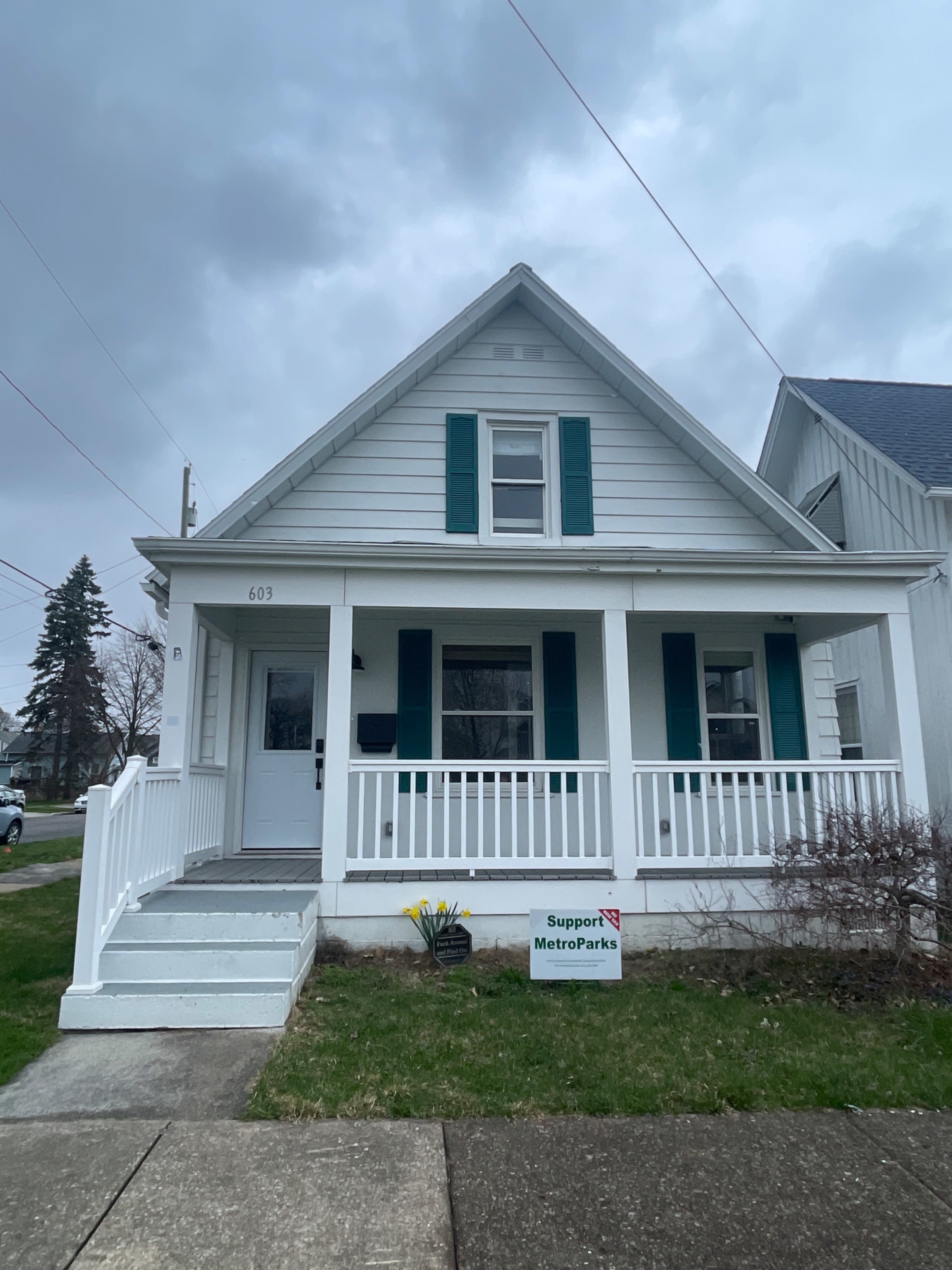 A two-story, white house with teal shutters and a front porch, located at 603, along with a sign supporting MetroParks in the yard.