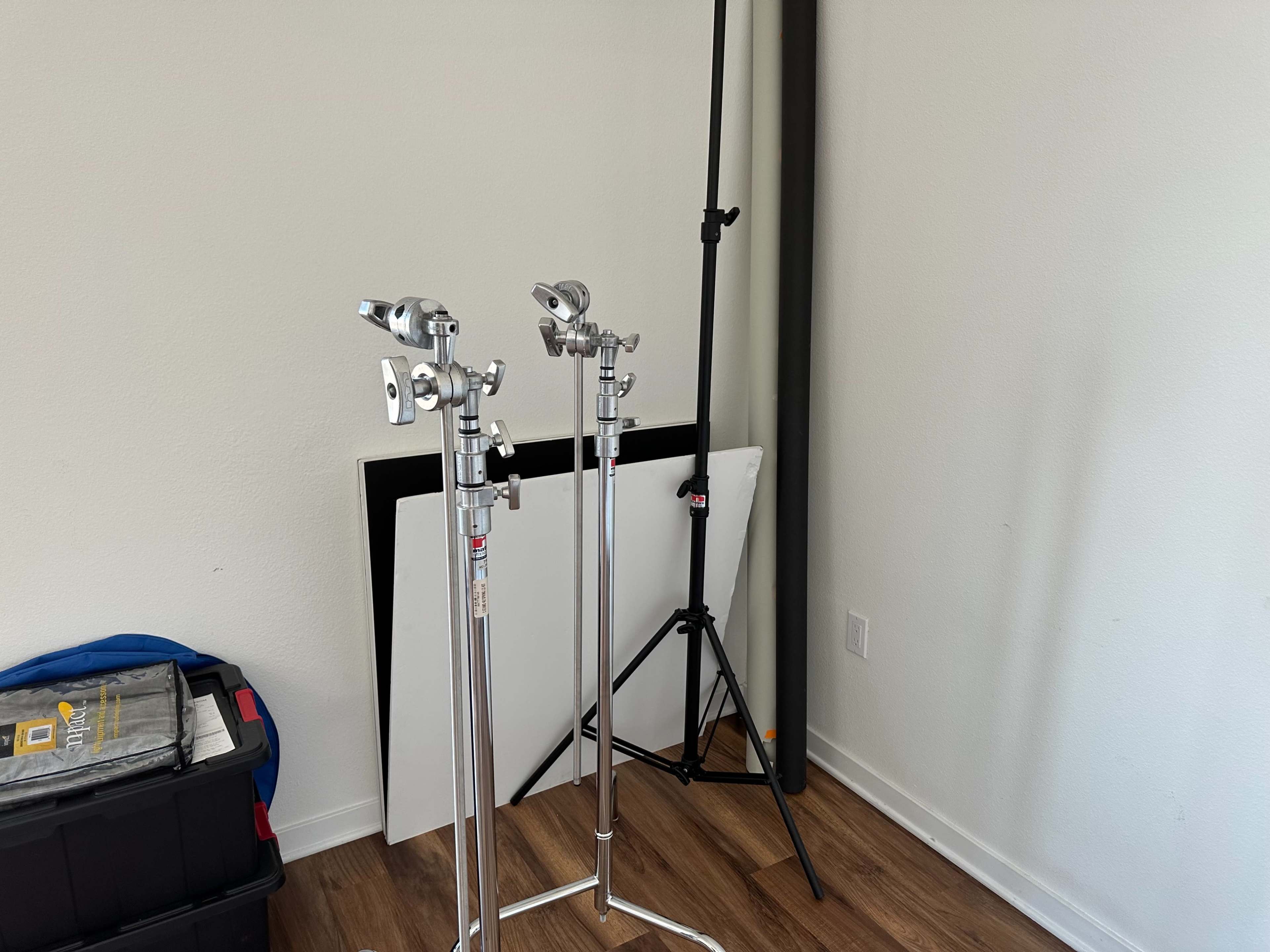 The image shows two metal light stands and a backdrop support in a room with wooden flooring and minimal furniture.
