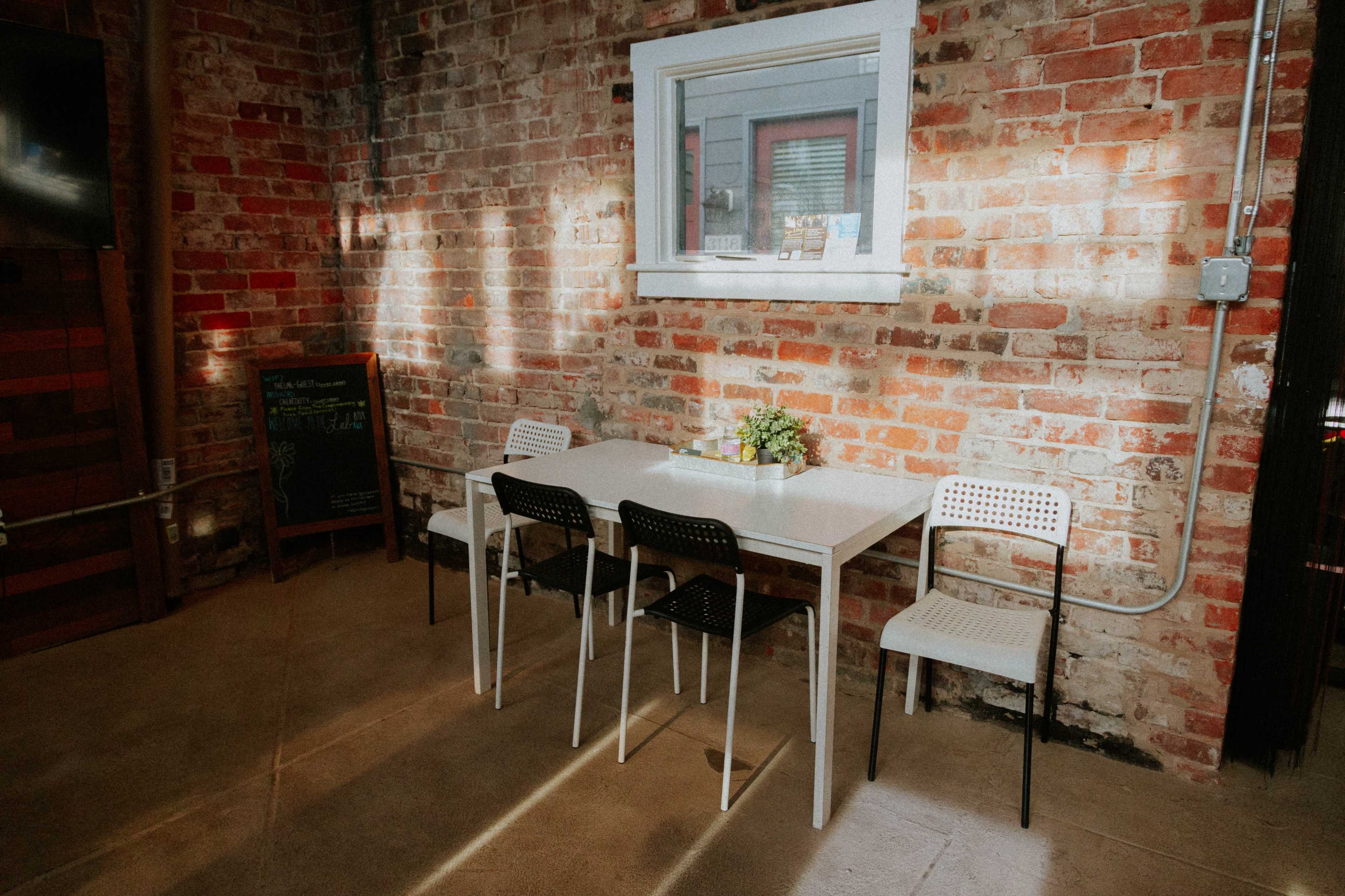A small table with four chairs is set against a brick wall, illuminated by natural light coming through a window.