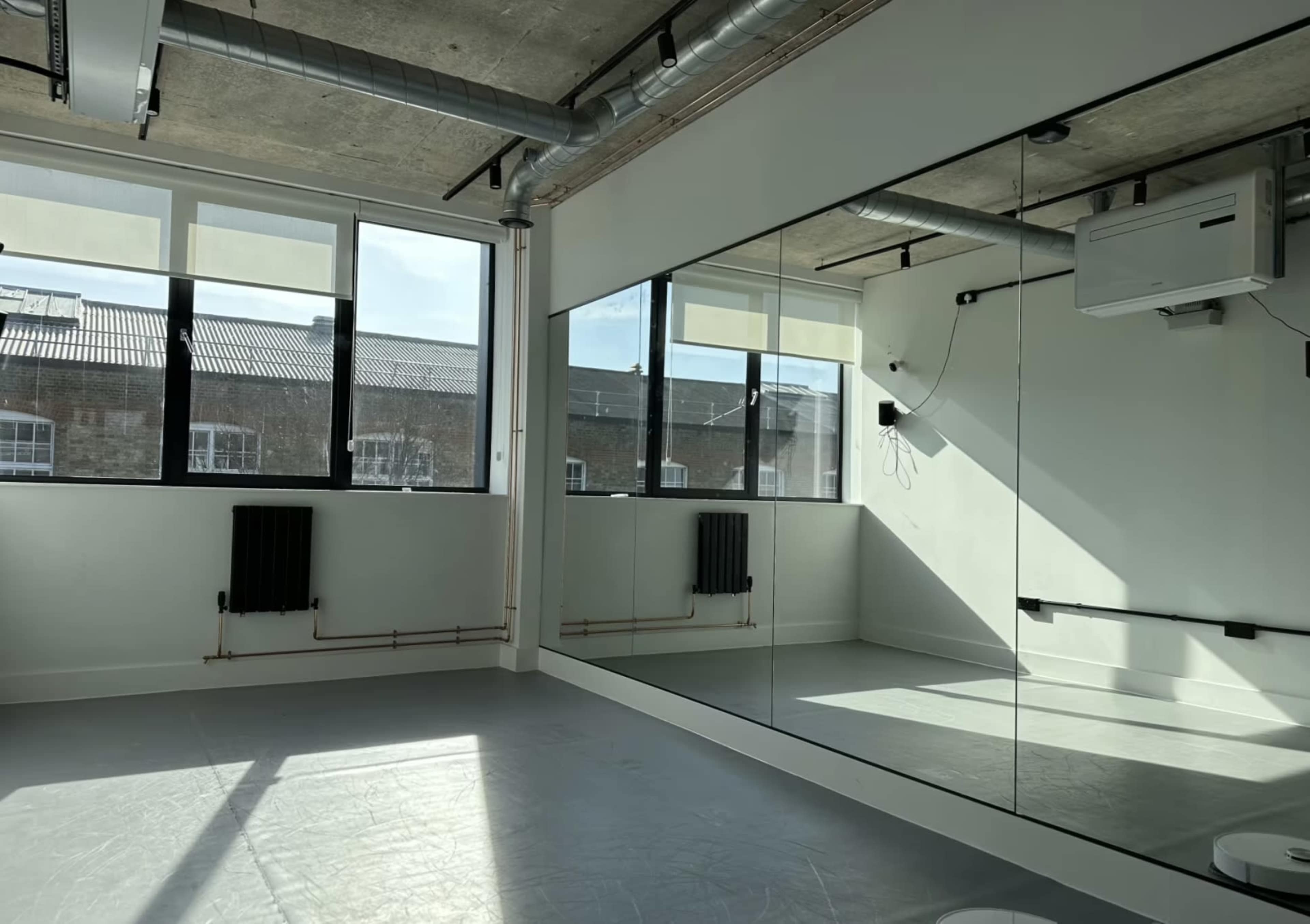 A bright, empty studio features large mirrors on one wall and ample natural light streaming through the windows.