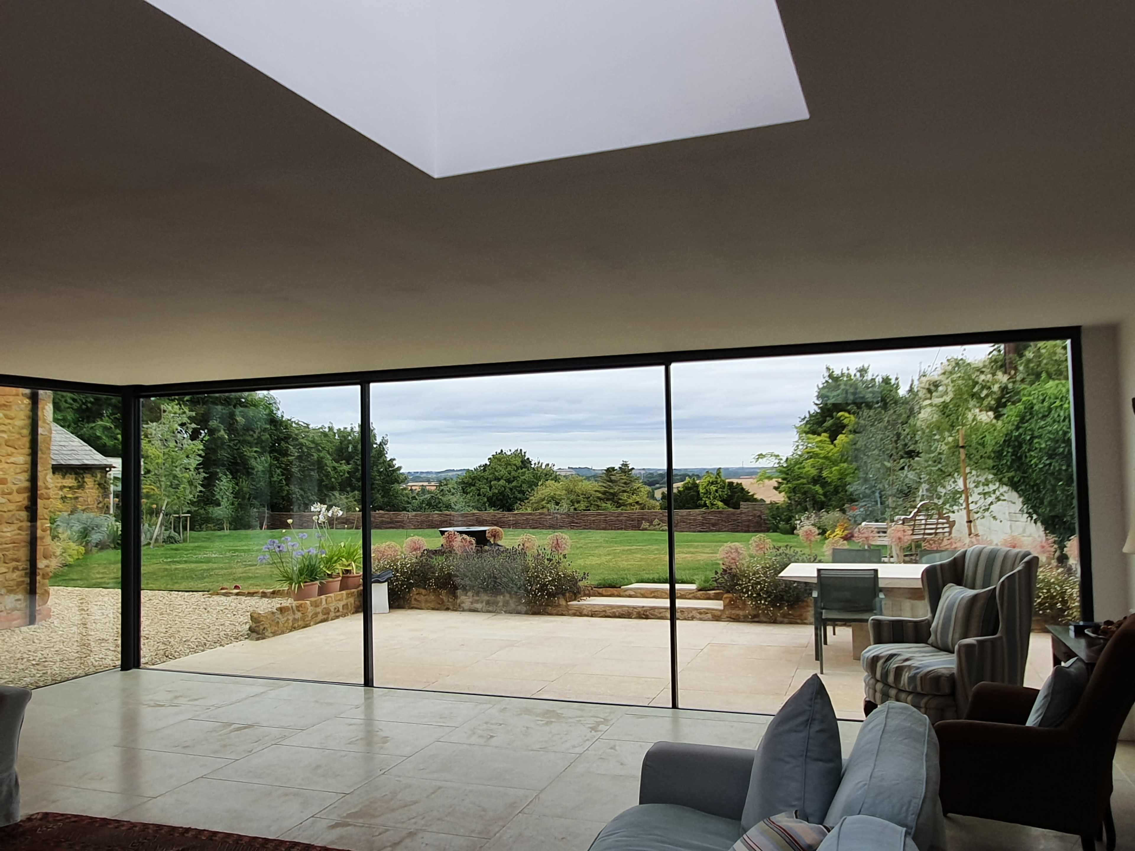 The image shows a modern interior space with large glass windows that offer a view of a grassy outdoor area and distant hills.