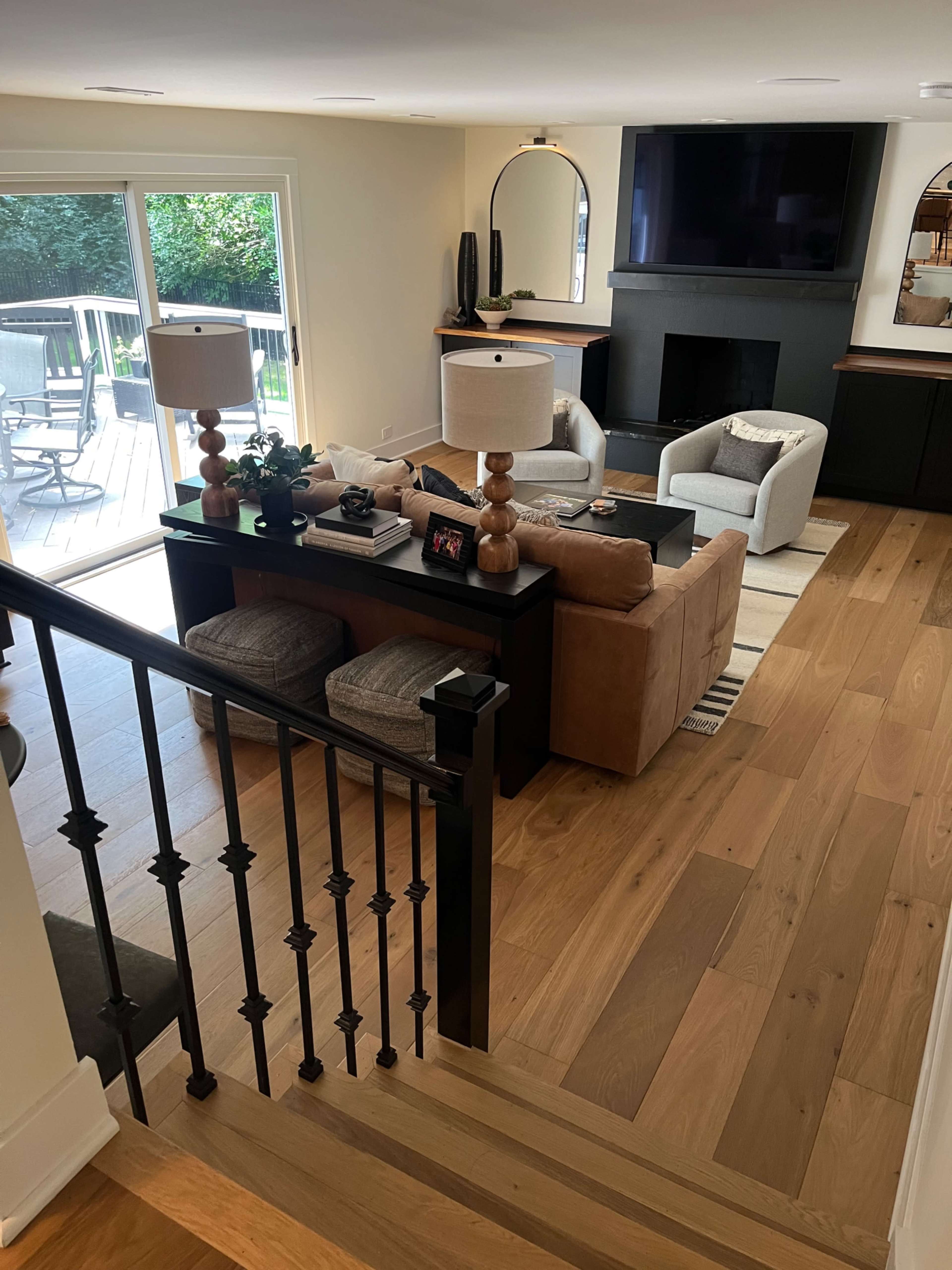 The image shows a modern living room with light wooden flooring, a dark fireplace, a large flat-screen television, and a sectional sofa arranged around a coffee table.