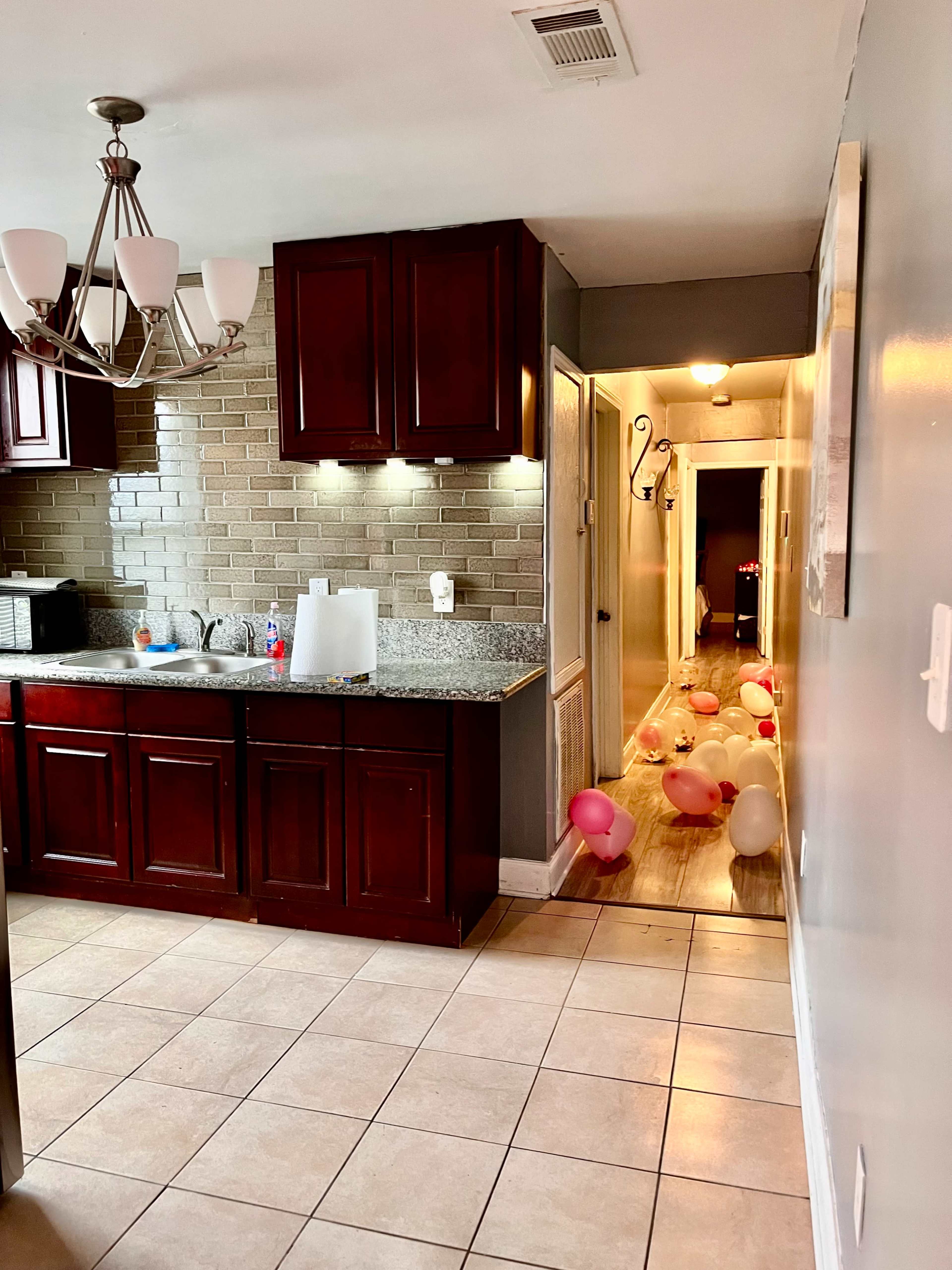 A kitchen with dark wood cabinets and granite countertops leads to a hallway decorated with colorful balloons on the floor.
