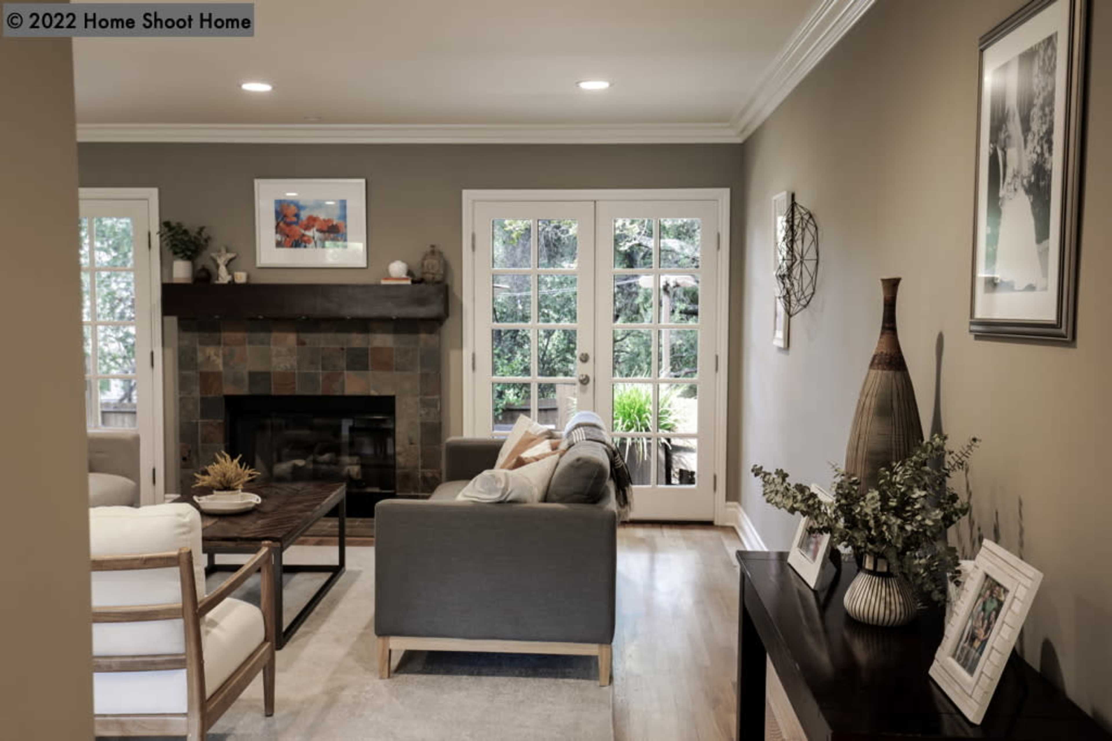 The image shows a living room with a fireplace, a coffee table, and large glass doors opening to an outdoor space.