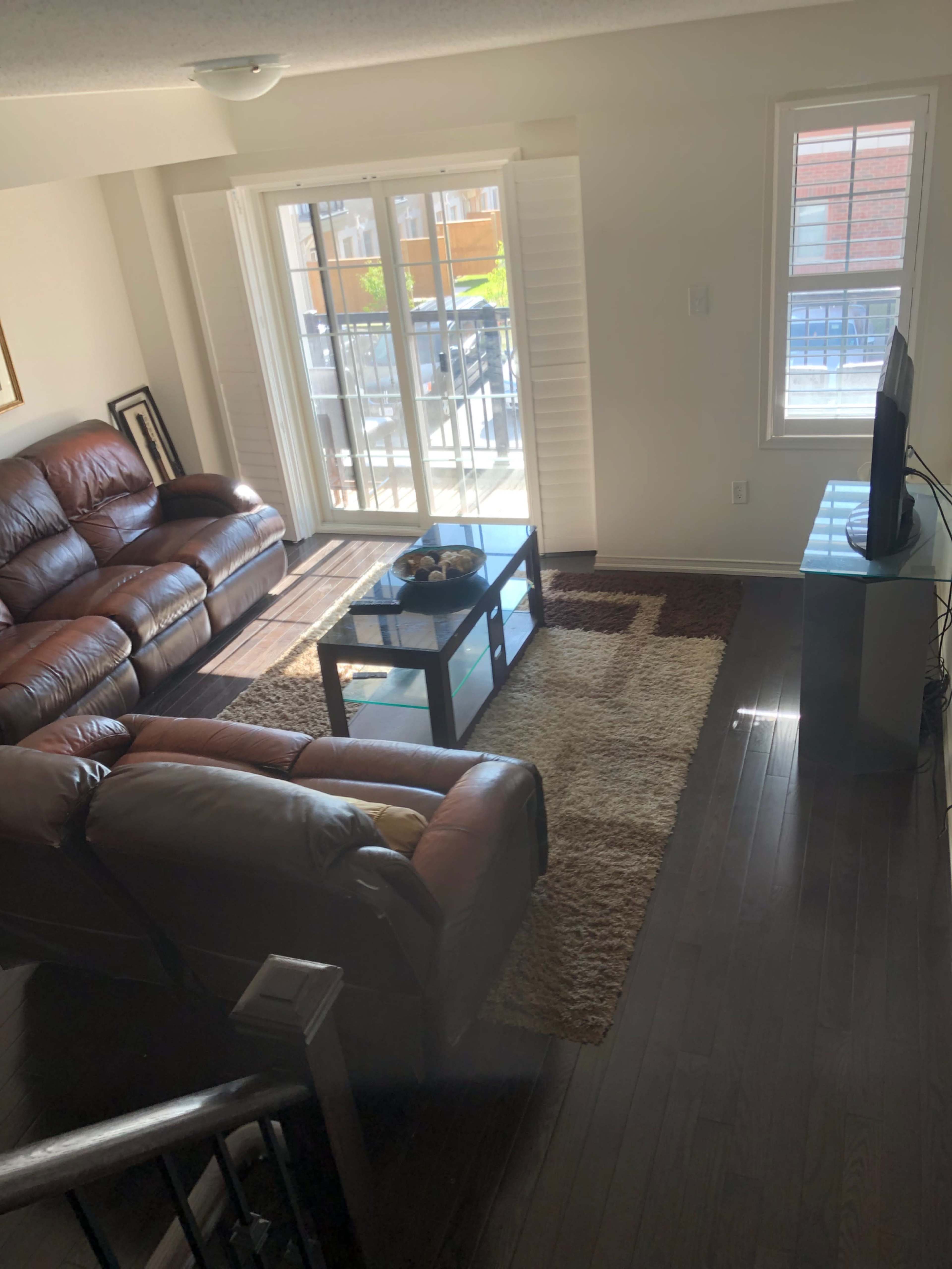 A living room with two dark leather sofas, a coffee table on a rug, and a television against a wall with windows letting in natural light.