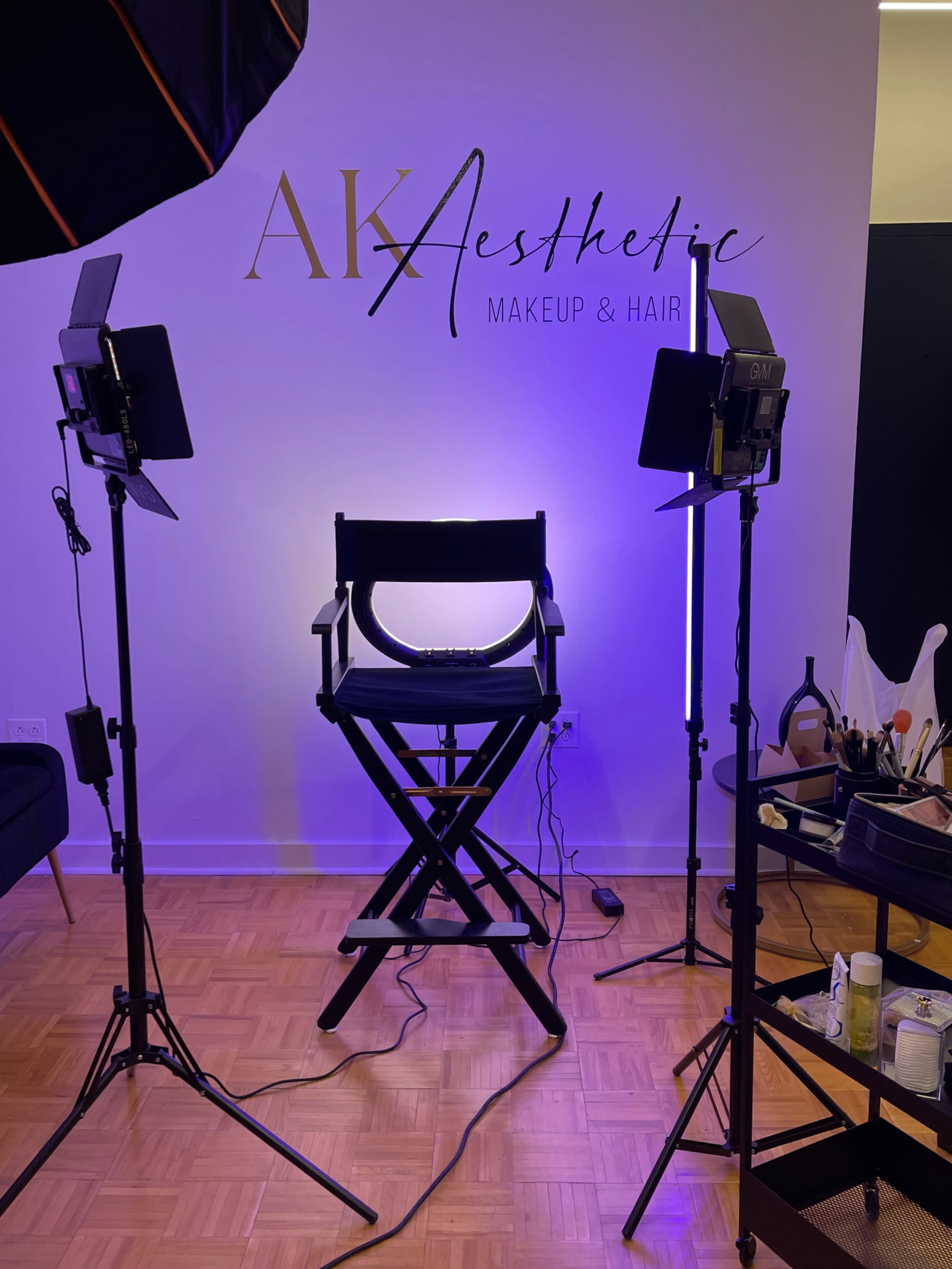 A makeup and hair studio with a director's chair positioned under soft lighting and surrounded by professional lighting equipment.