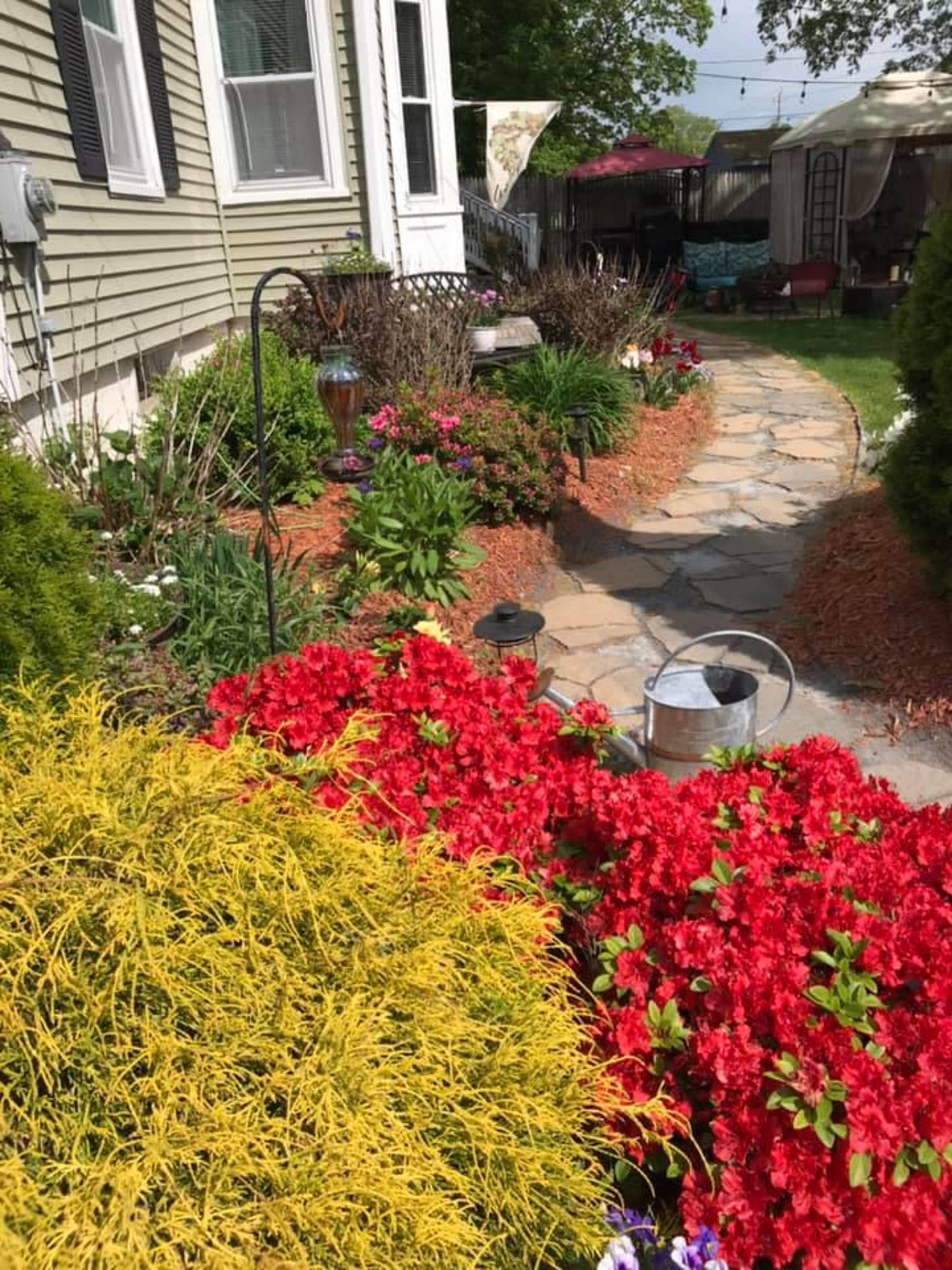 The garden features a stone path lined with vibrant flowers and greenery leading to a cozy home.