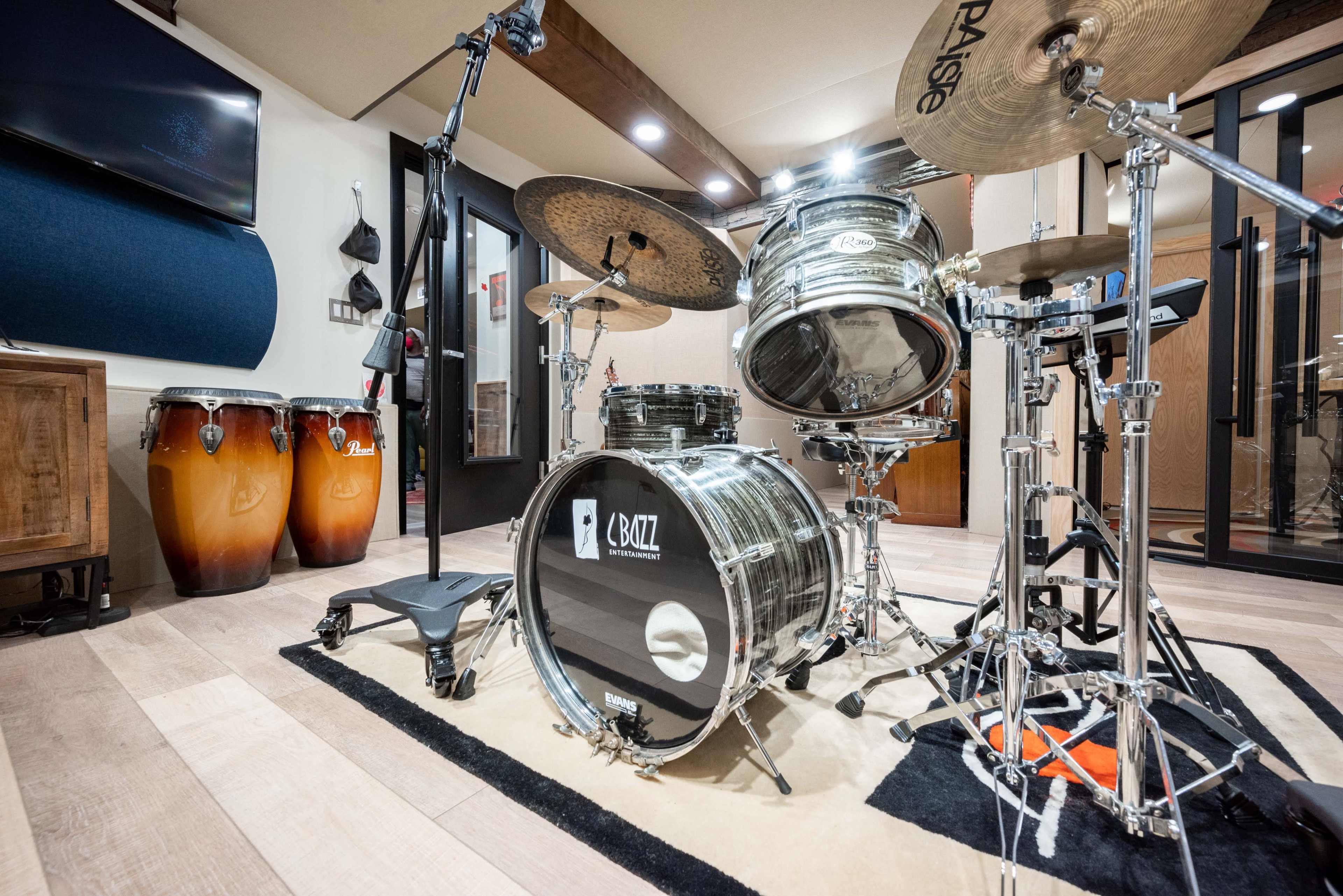 A modern drum set positioned in a music studio, accompanied by conga drums and a microphone stand.