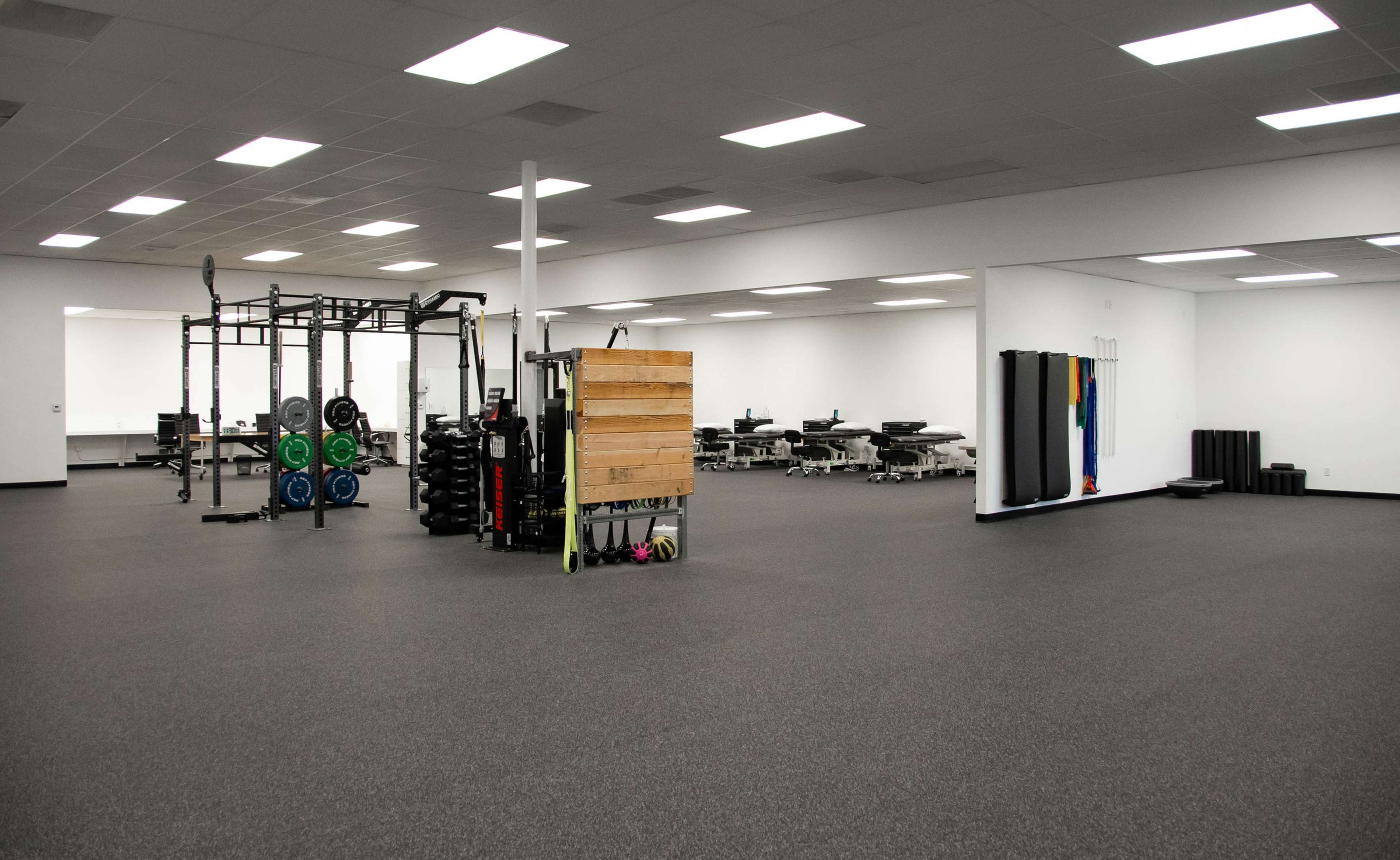 A spacious gym interior with weightlifting equipment, exercise mats, and workout stations arranged neatly on a dark floor.