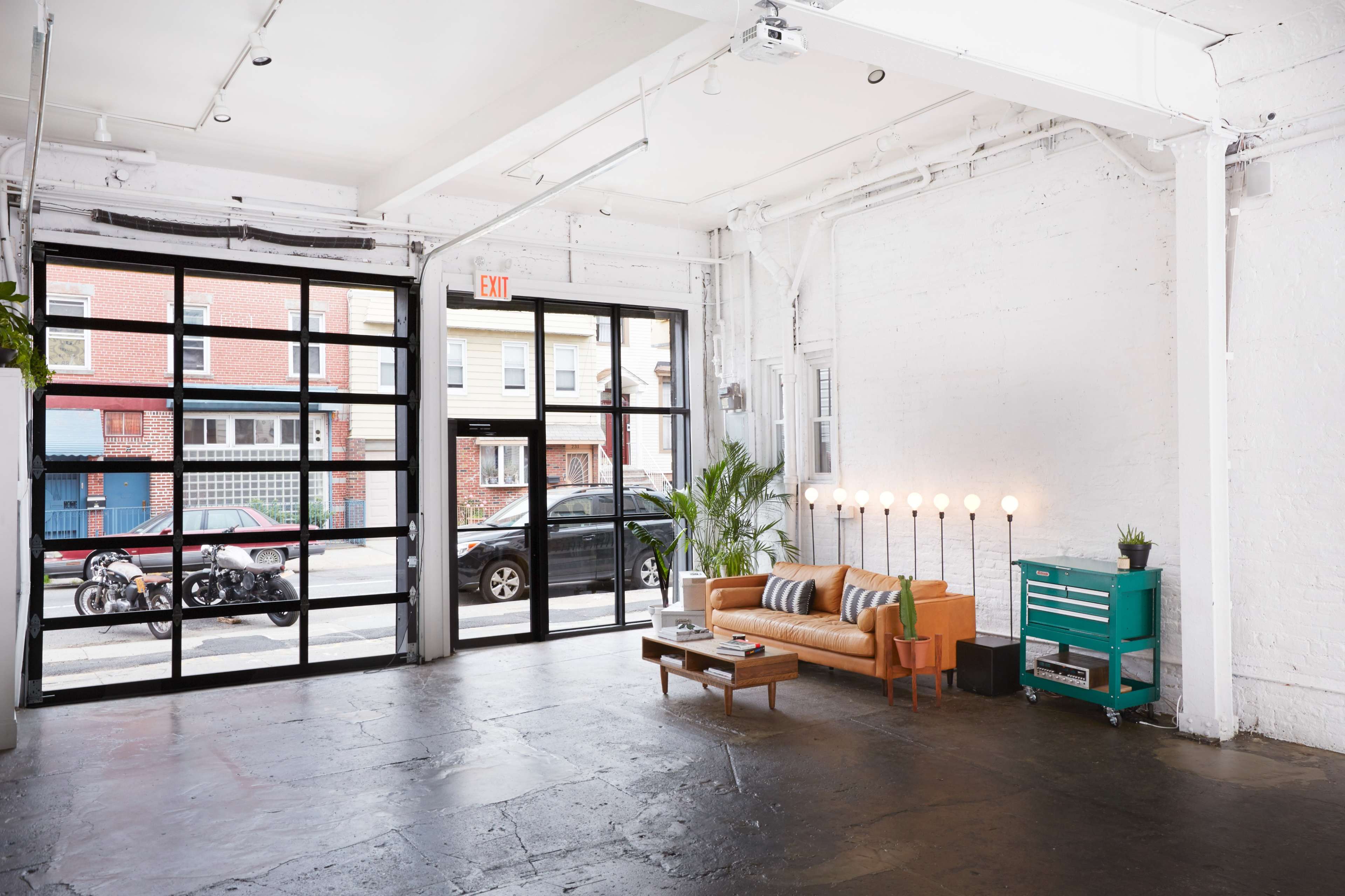 The image shows a bright, modern interior of a commercial space with a large glass door, a sofa, and a row of light fixtures.