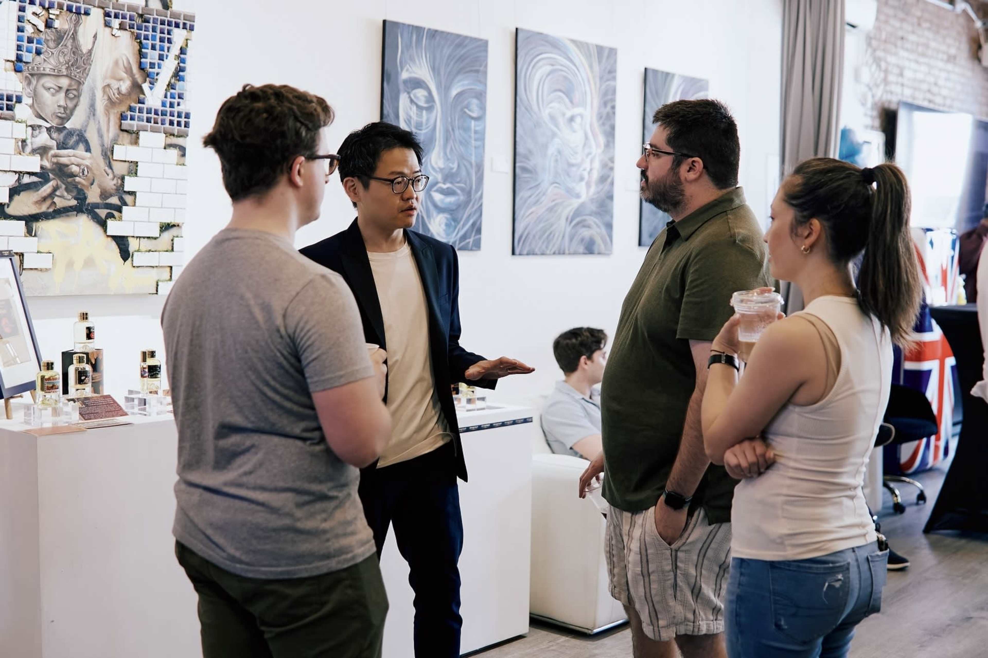A group of four people engage in conversation in a modern art gallery, with paintings visible on the wall behind them.