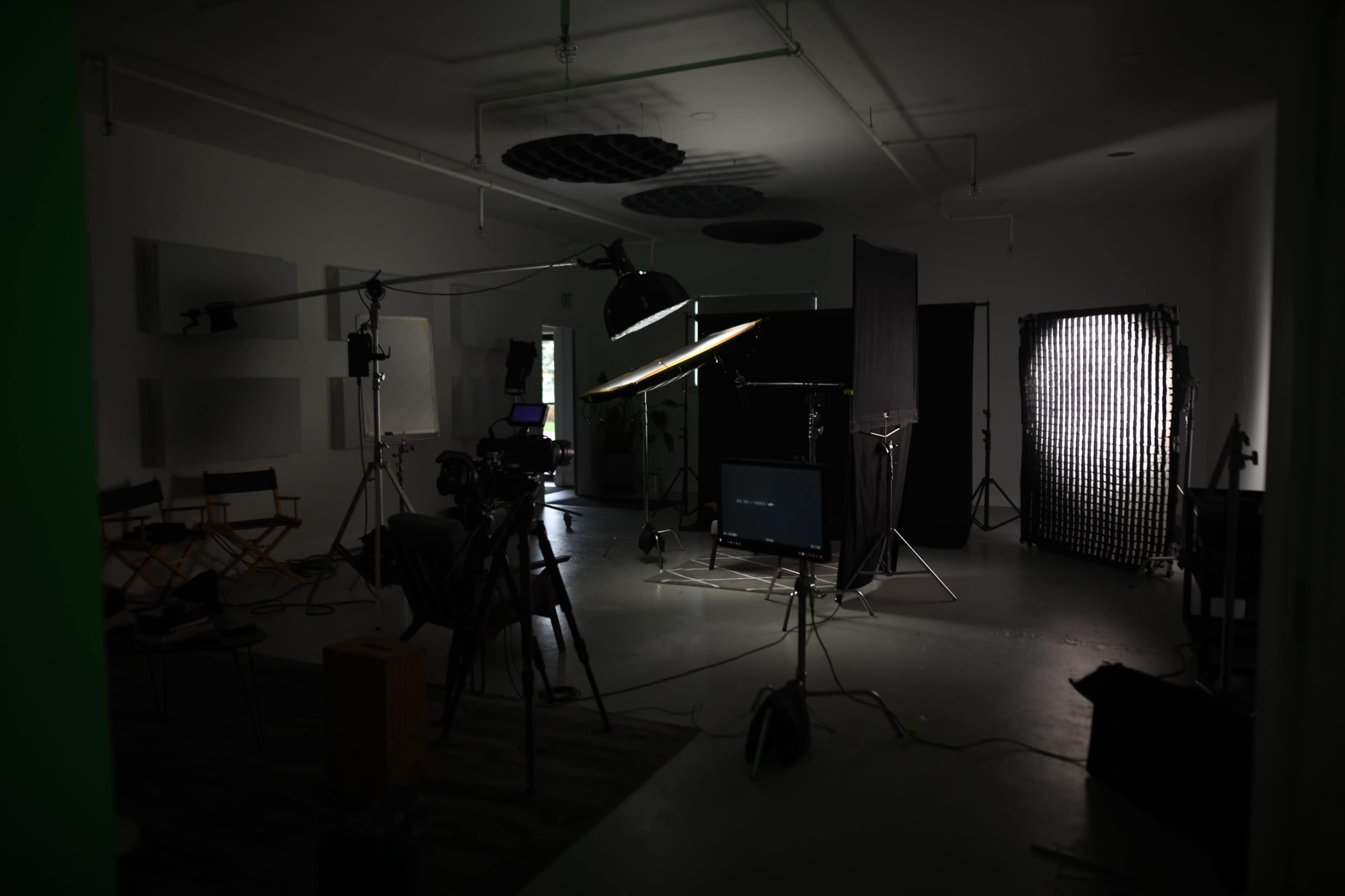 A dimly lit studio equipped with various lighting setups, cameras, and a backdrop for video production.
