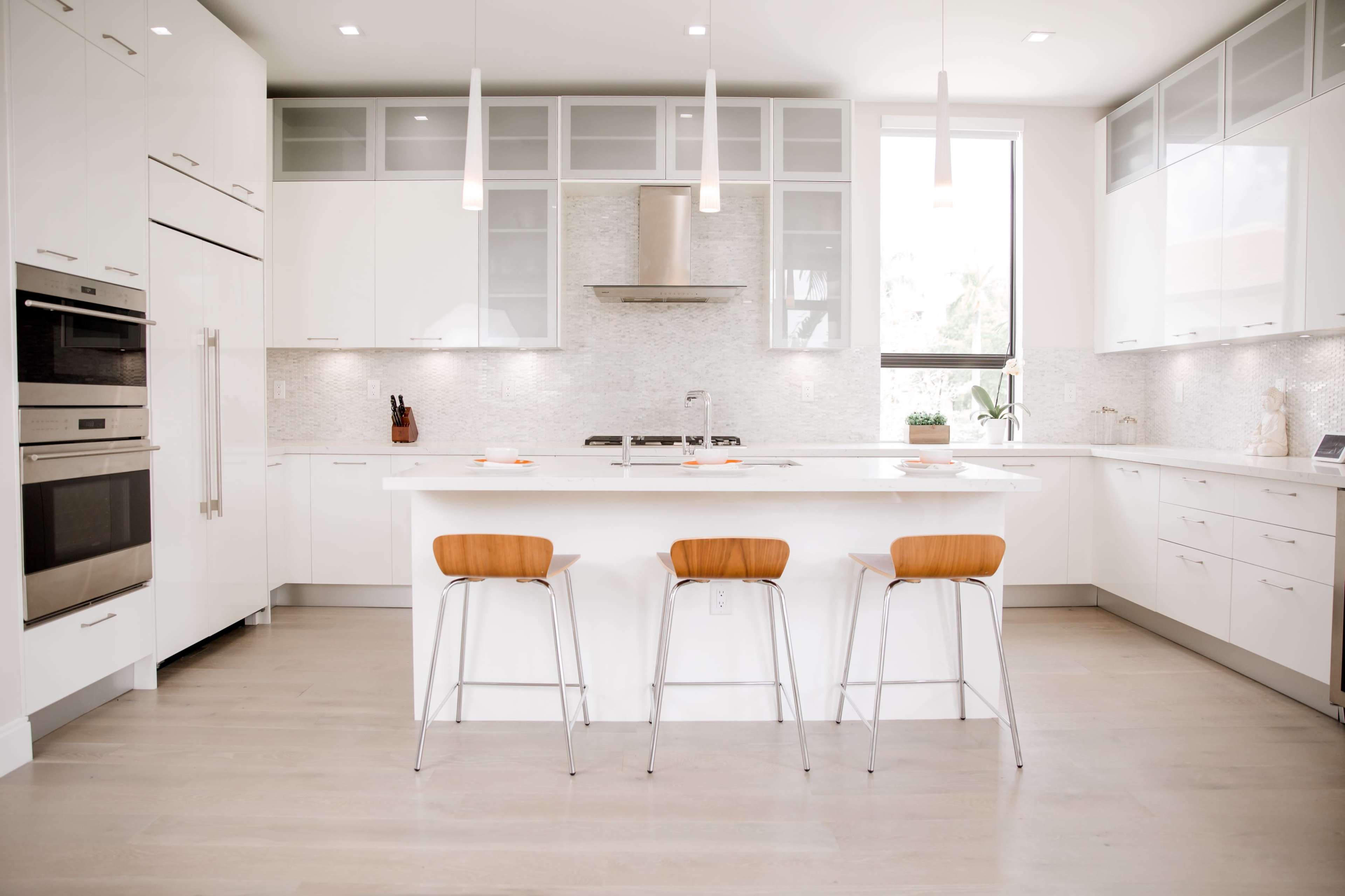 A modern kitchen features white cabinetry, stainless steel appliances, and a large island with three wooden bar stools.