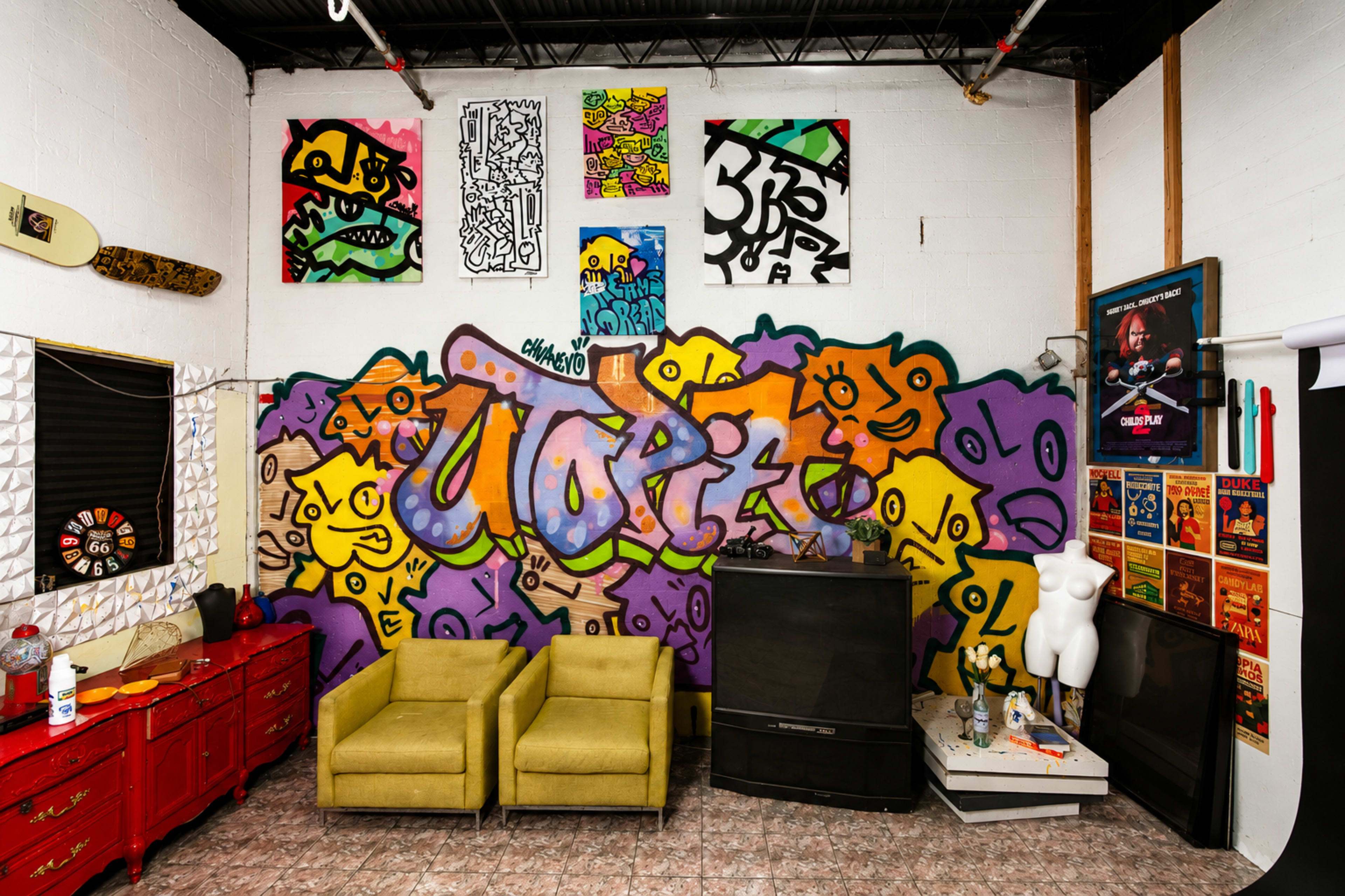 The scene features a vibrant wall covered in graffiti art, with two yellow chairs in front and a television set beside a mannequin and various framed artworks.