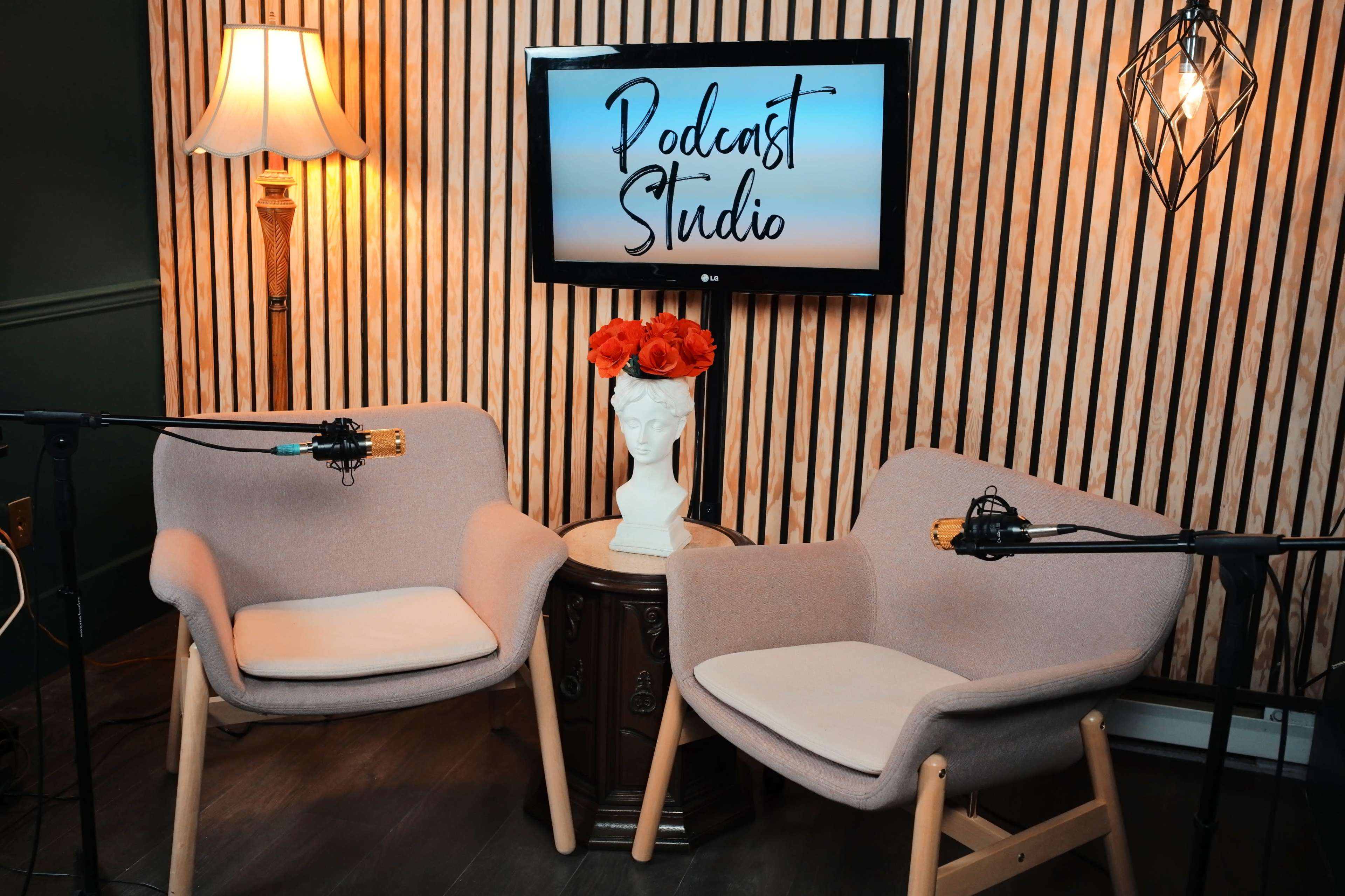 The image shows a podcast studio setup with two chairs, a decorative table, a television displaying "Podcast Studio," and a vase of orange flowers.