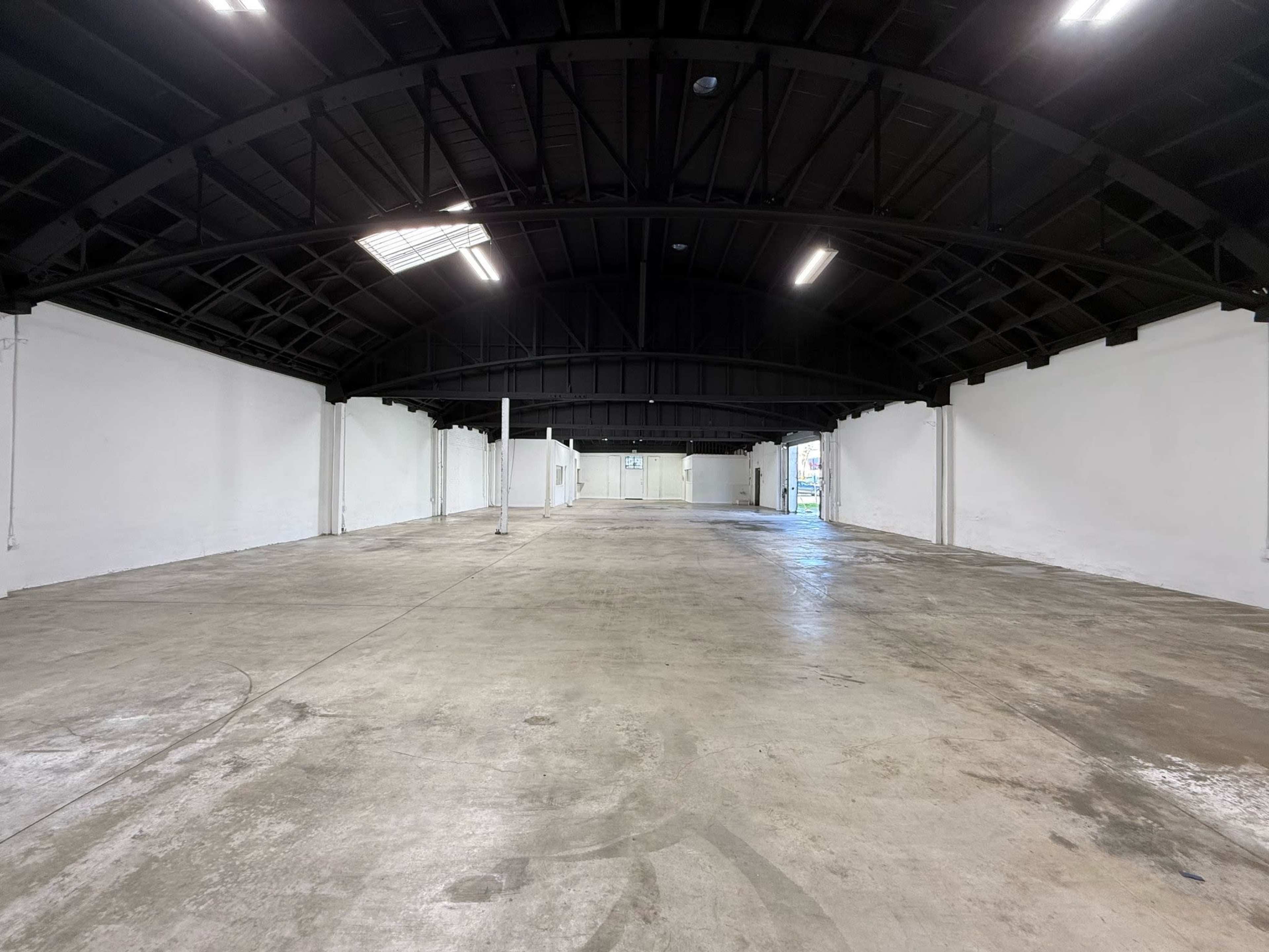 The image shows an empty industrial warehouse space with a high black ceiling and white walls.