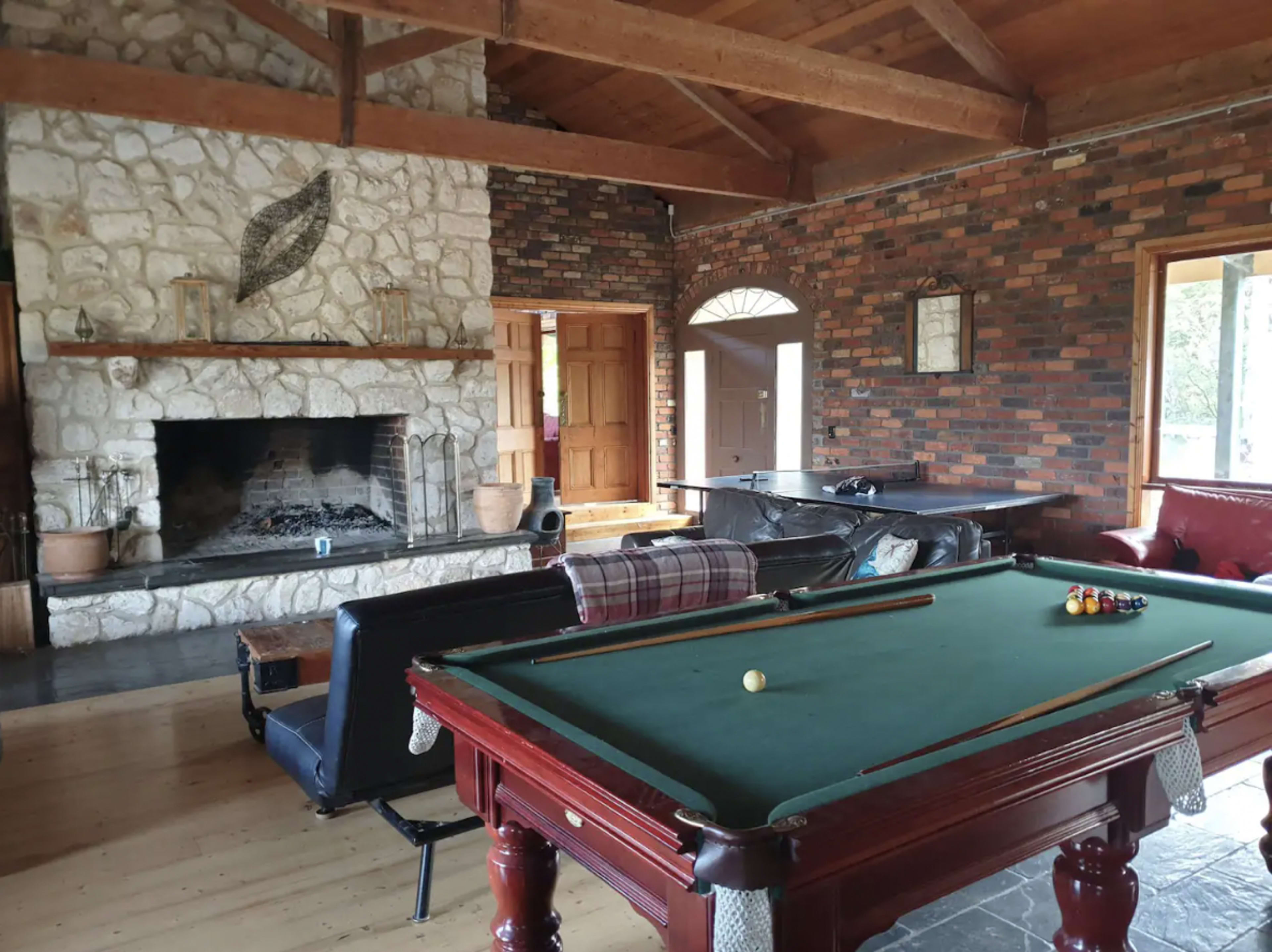 A spacious interior with a billiard table, a stone fireplace, and wooden beams overhead.