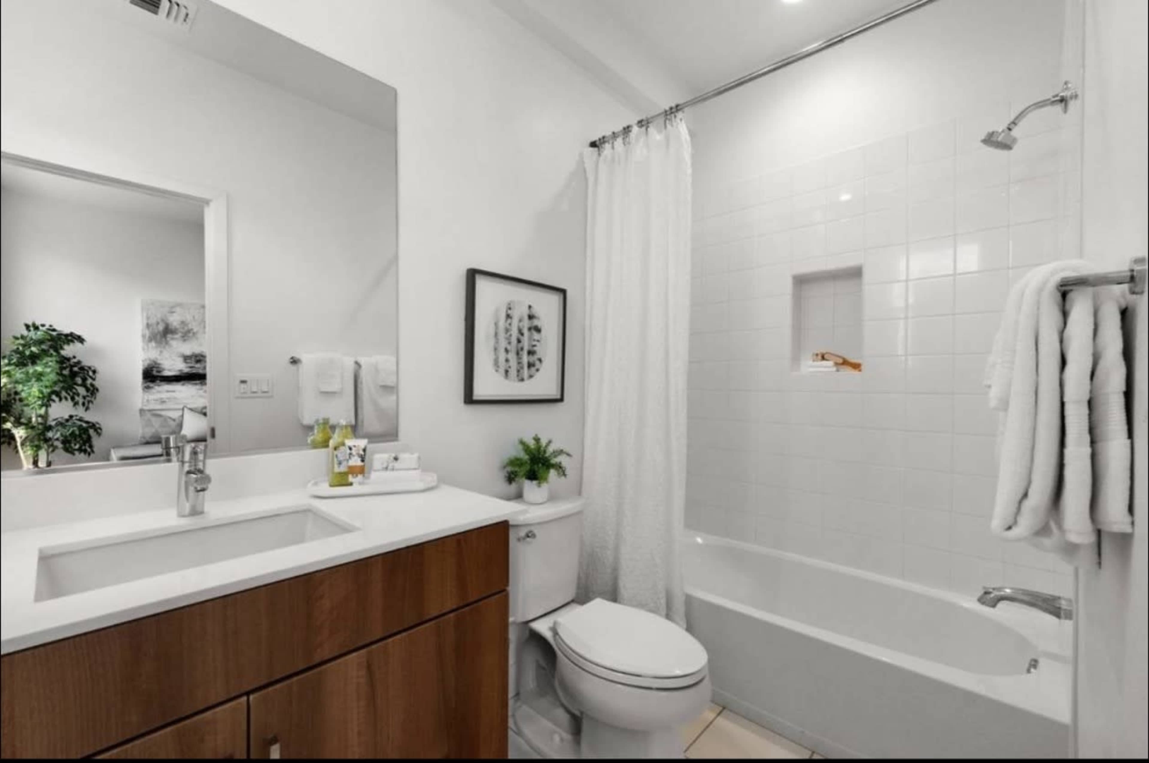 The image shows a modern bathroom with a shower and tub combination, a white countertop, a wooden vanity, and a large mirror.