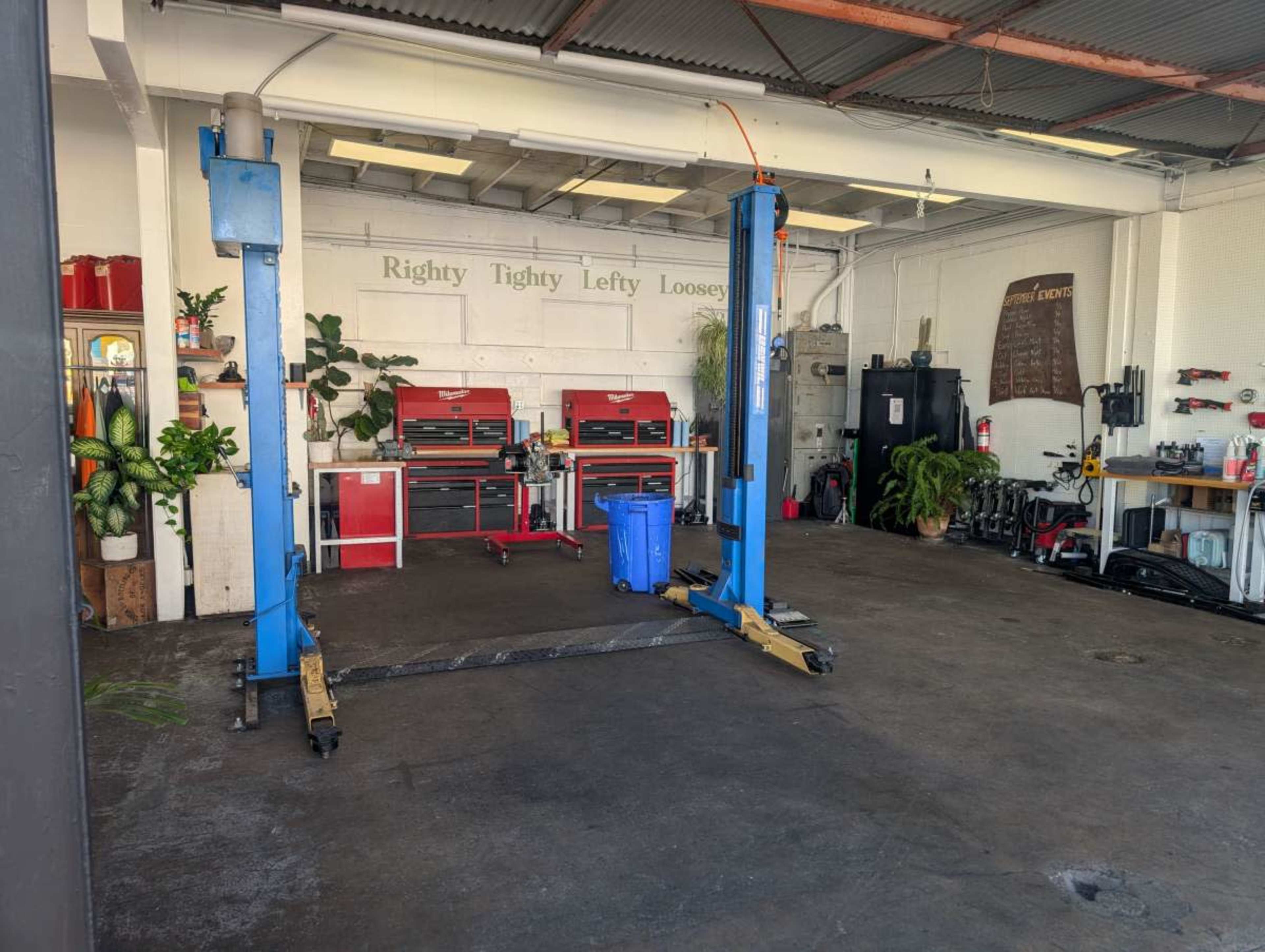 The image shows an auto repair shop with two blue hydraulic lifts, toolboxes against the wall, and various equipment arranged throughout the space.