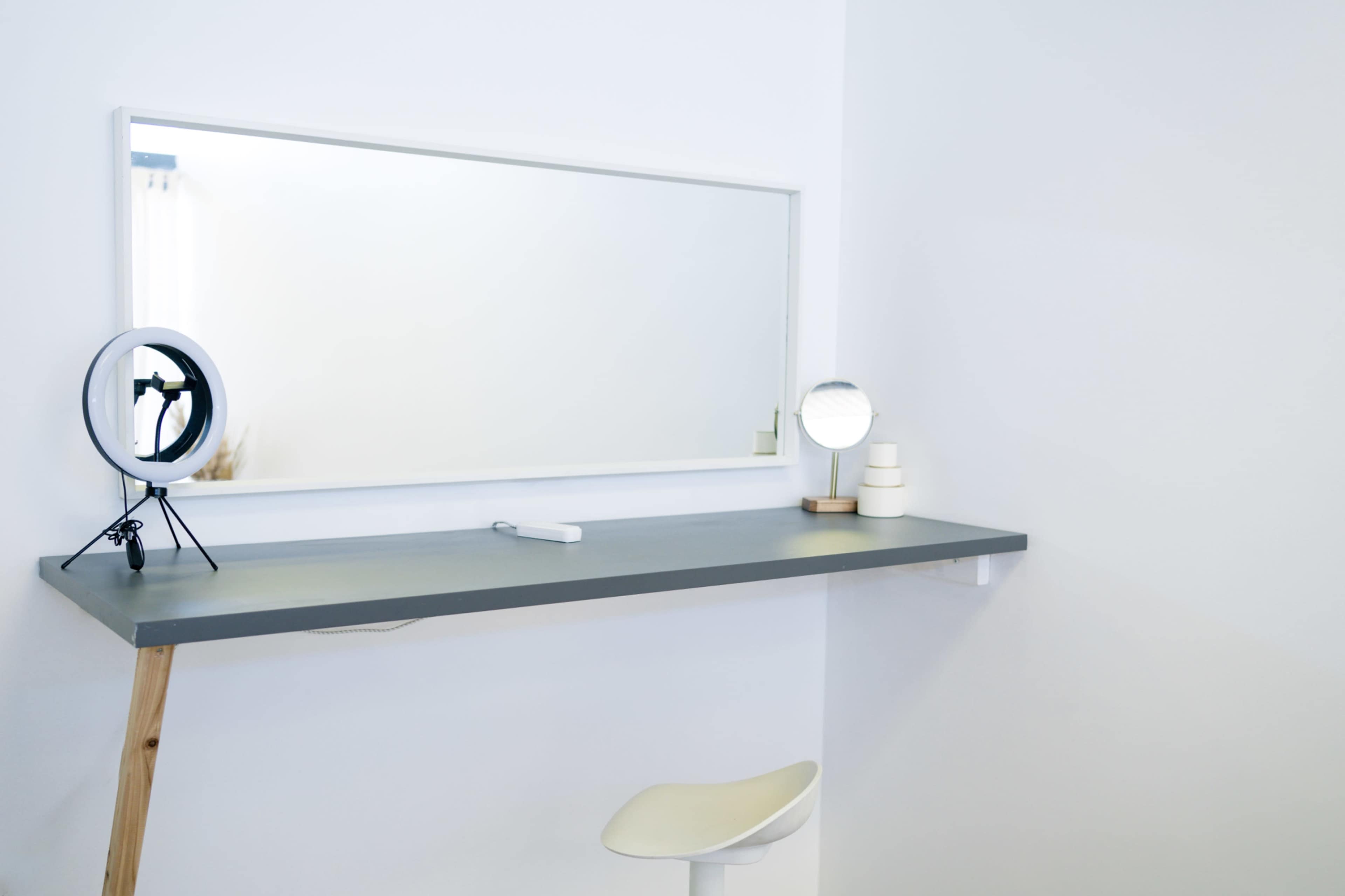 The image shows a minimalistic vanity area with a simple gray countertop, a large mirror, and two distinct circular mirrors on either side.