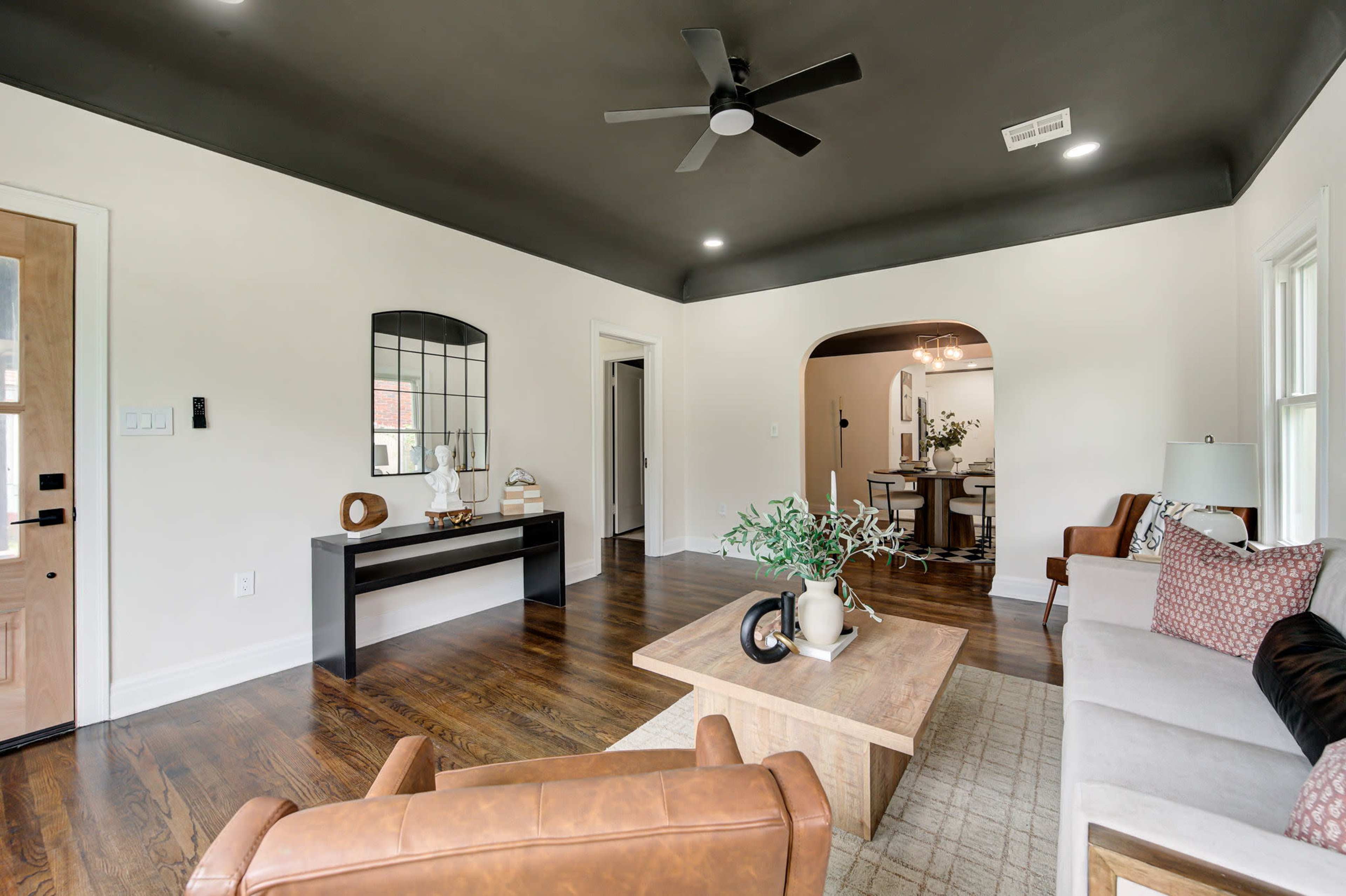 The living room features a brown leather chair, a wooden coffee table, and a mirror above a console table, with a view into an adjoining dining area.