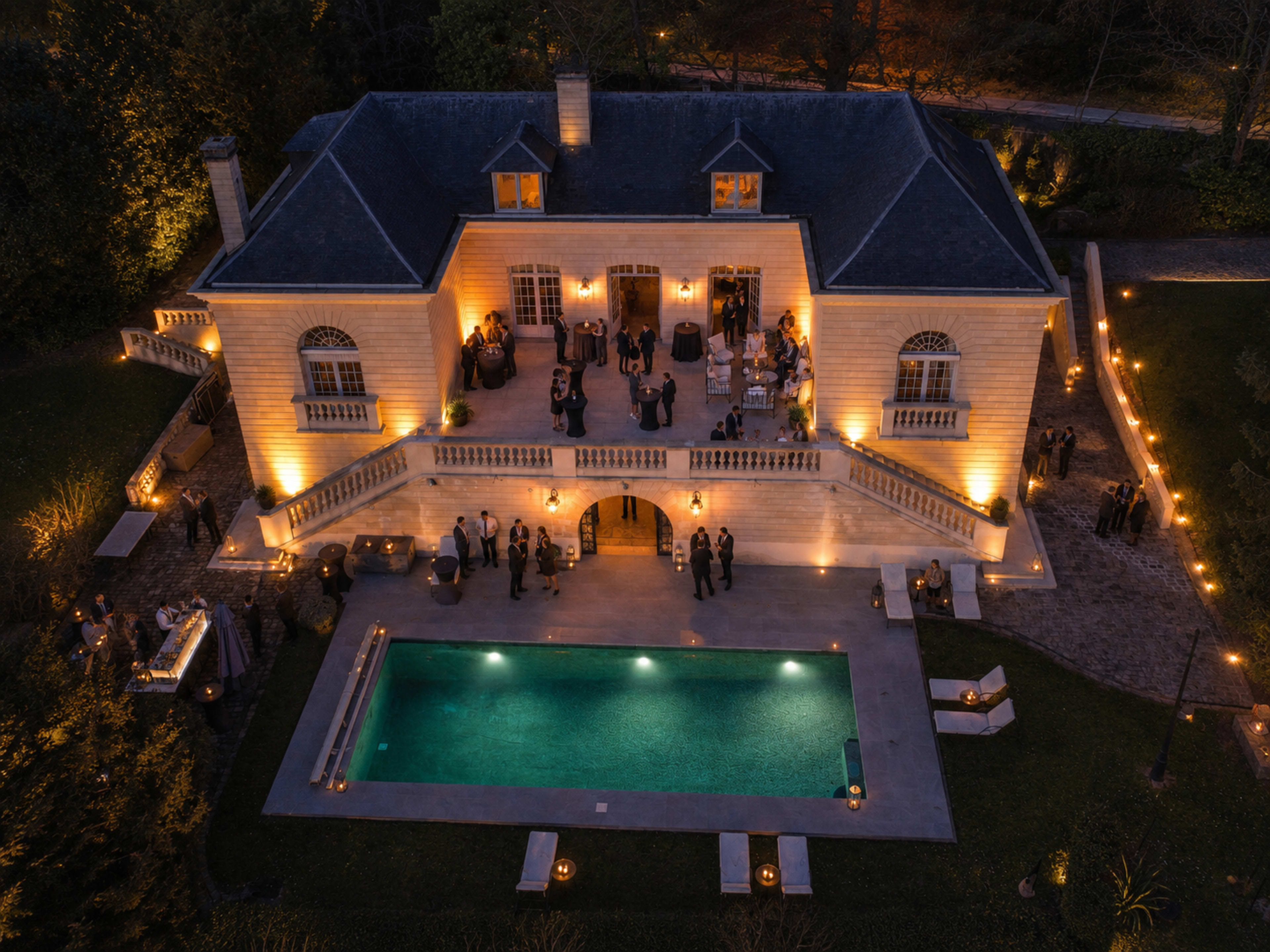 An elegant house with illuminated outdoor spaces and a pool hosts a gathering of people.