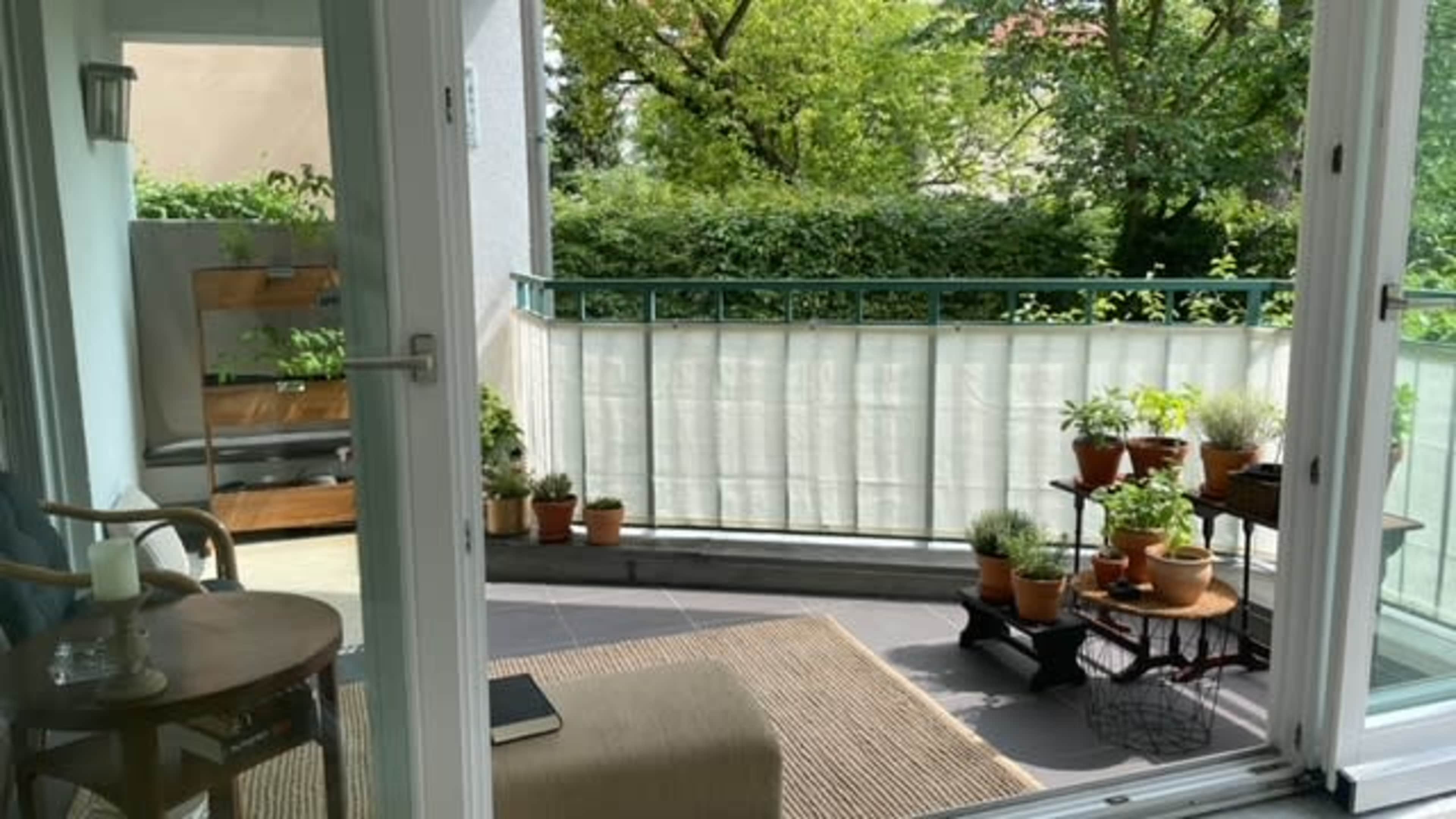 A balcony with potted plants and a small seating area, viewed through large glass doors.