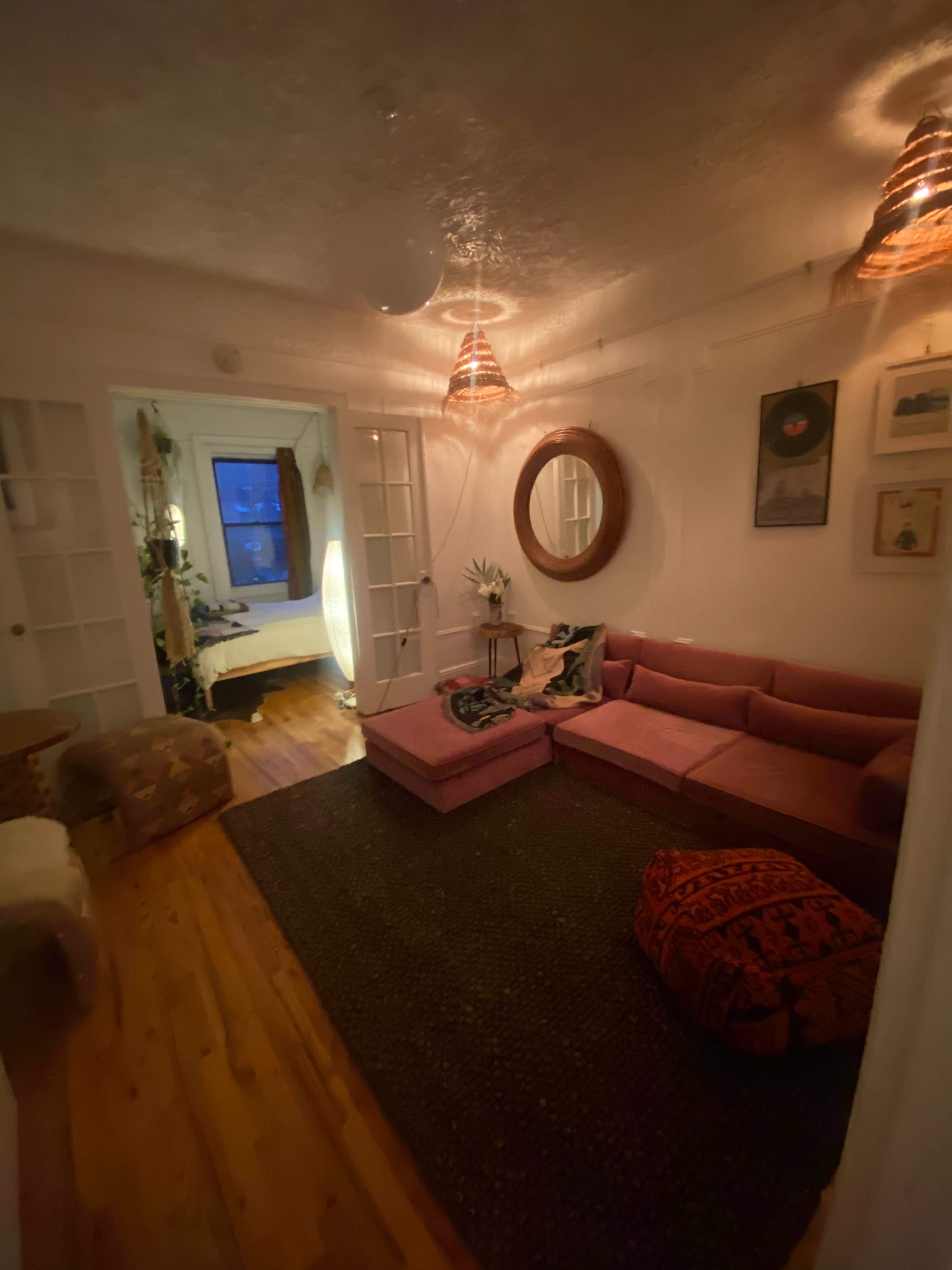 A cozy living room with a pink sectional sofa, a round mirror on the wall, and soft lighting creating a warm atmosphere.
