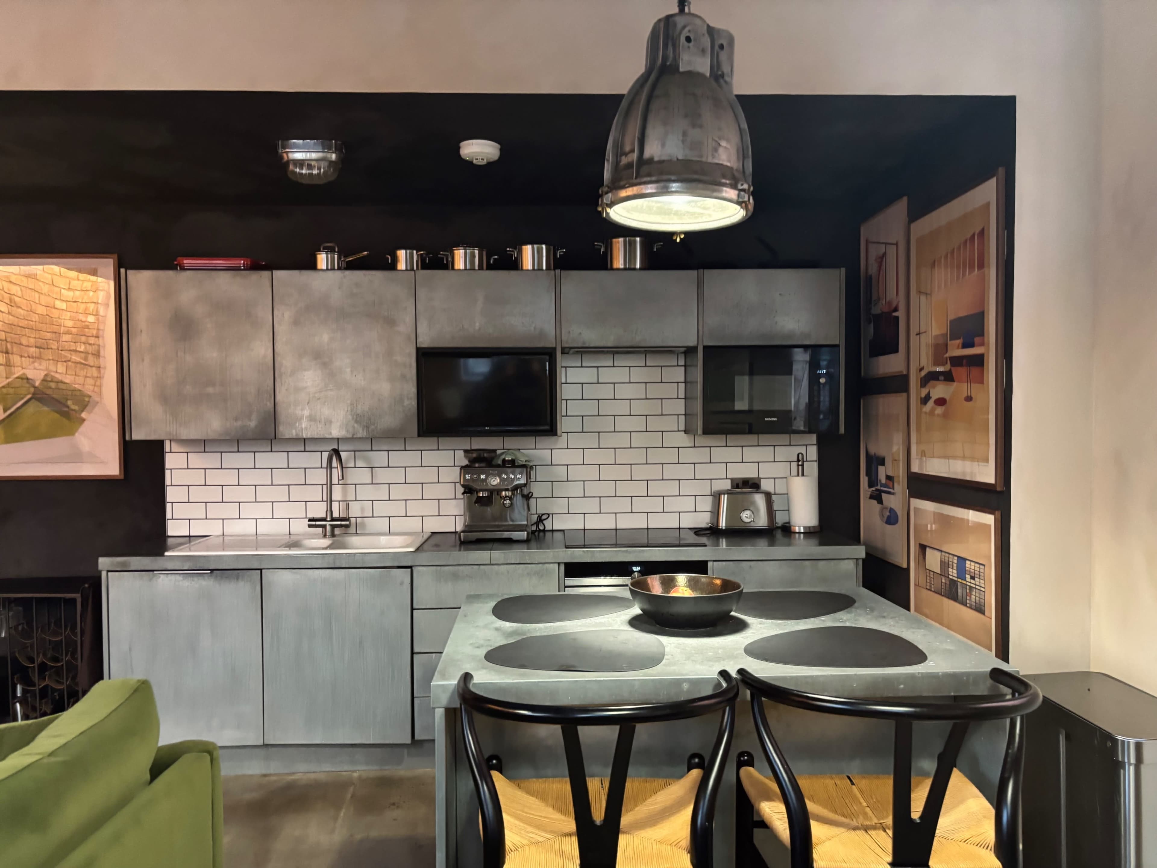 The image shows a modern kitchen with a metallic gray finish, equipped with a stove, microwave, and sleek cabinetry, along with a dining table and black chairs.