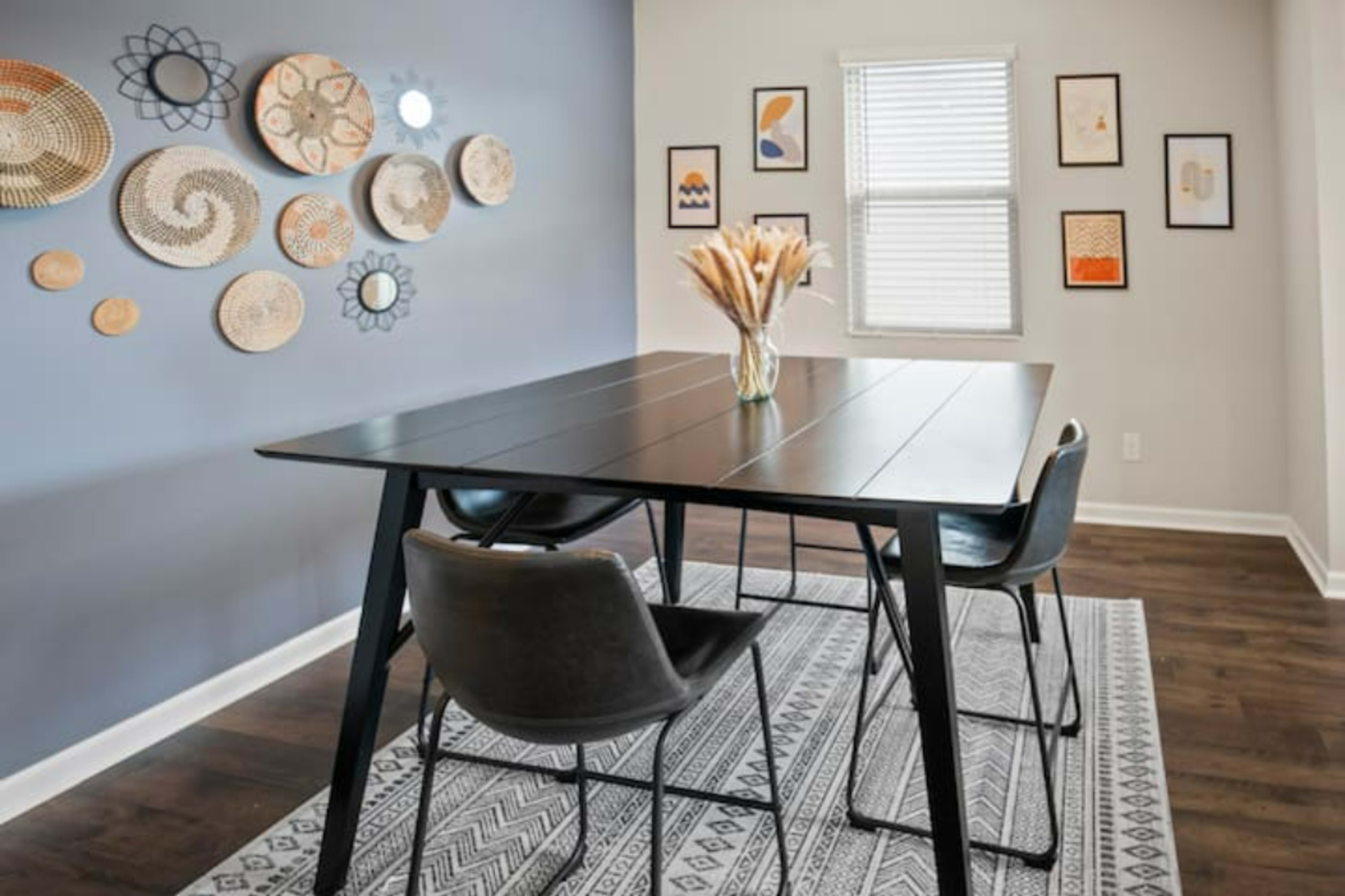 A dining area features a black table with three chairs, surrounded by patterned wall decor and a light-colored rug.