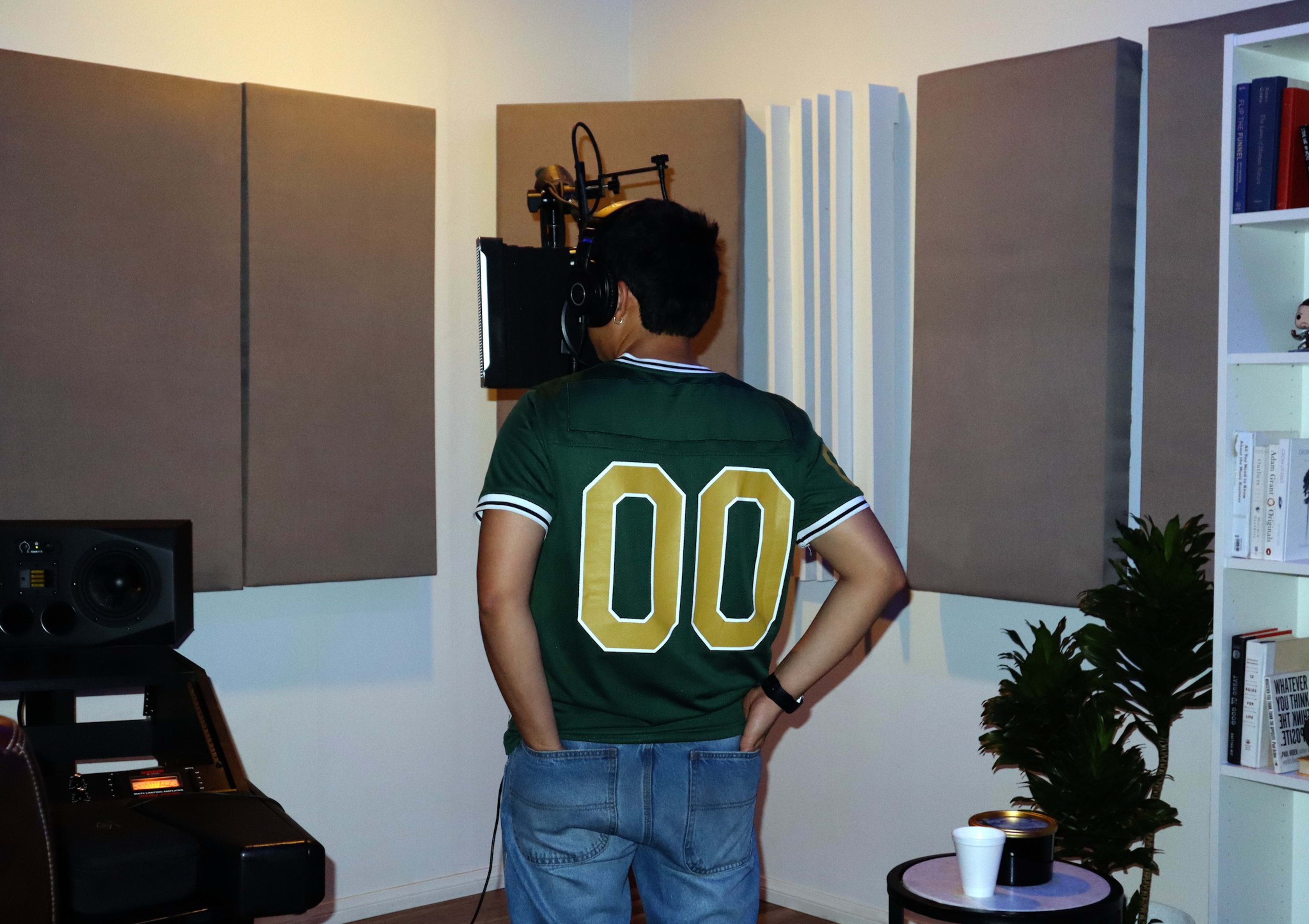 A person wearing a green jersey with the number "00" stands in a recording studio, facing a microphone.