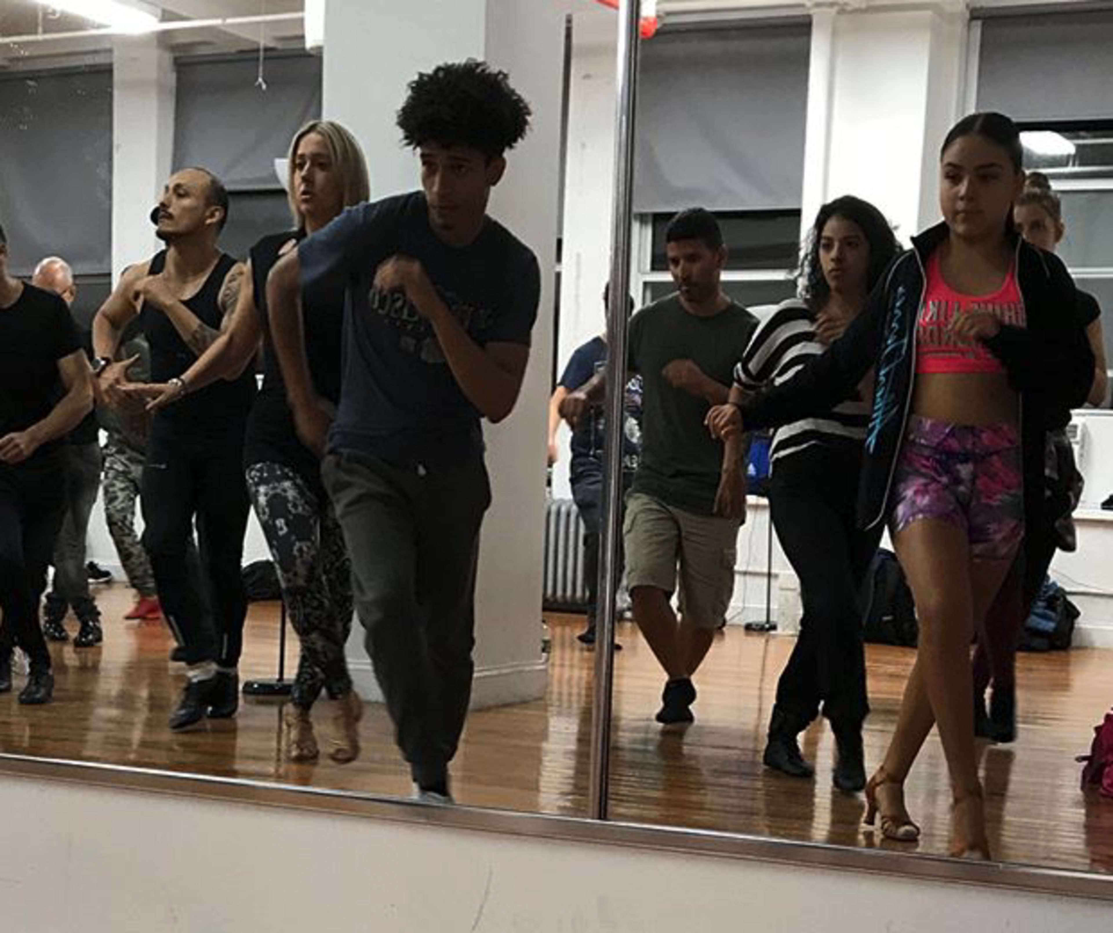 A group of diverse dancers practices choreography in a studio mirrored wall.