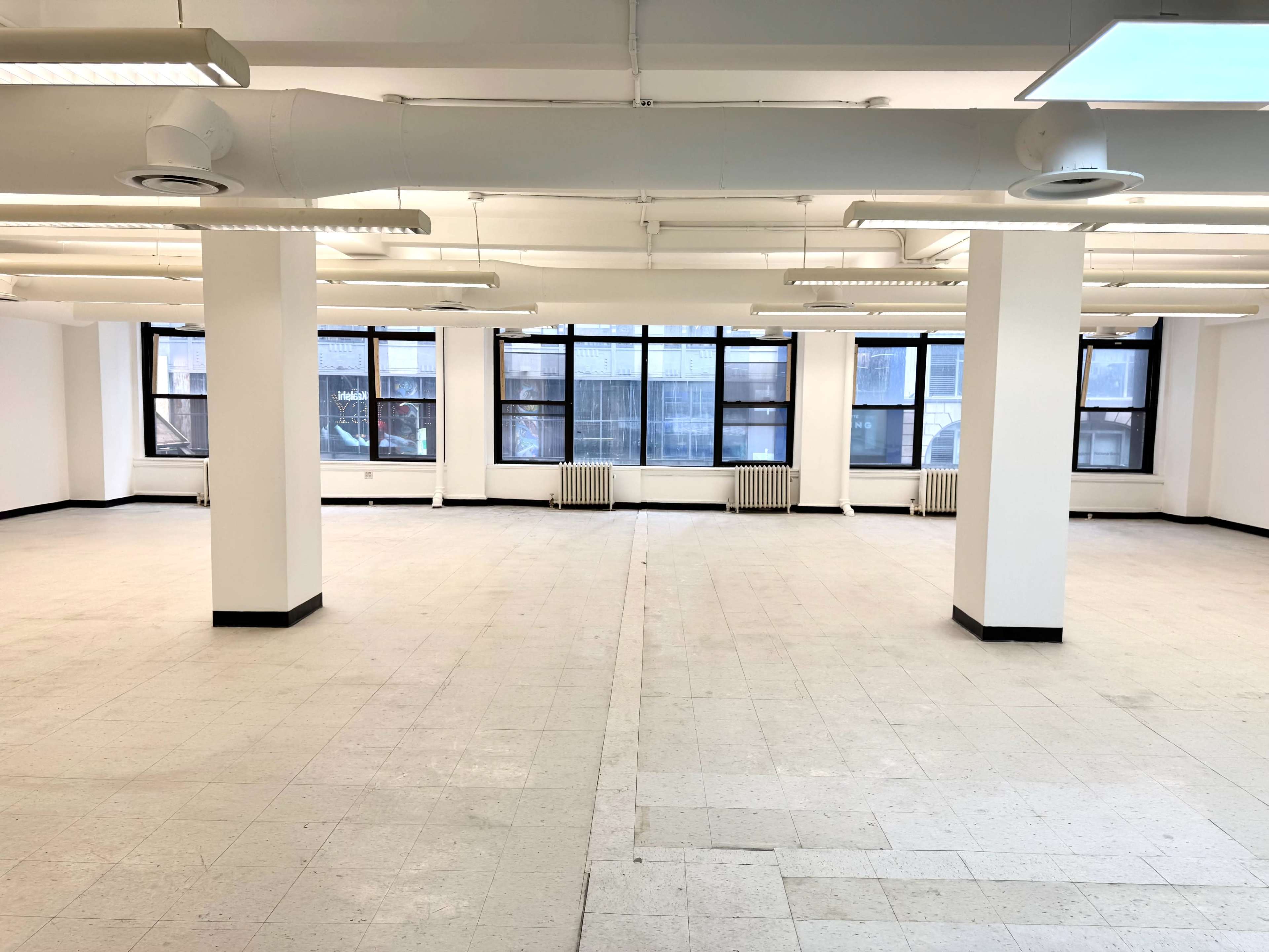 The image shows a spacious, empty office interior with large windows and white walls.