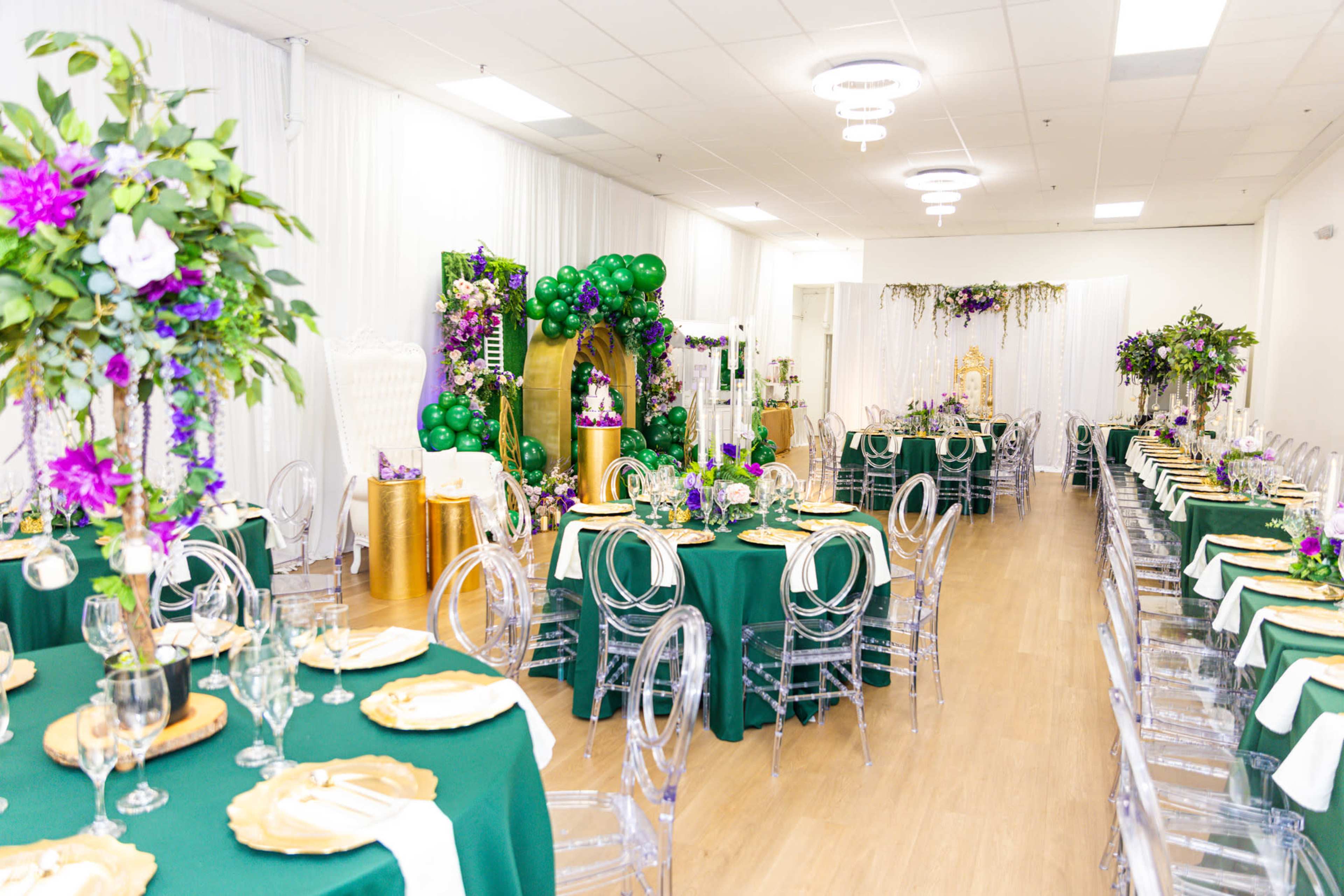 The image shows a decorated banquet hall with green tablecloths, clear chairs, and floral arrangements set for an event.
