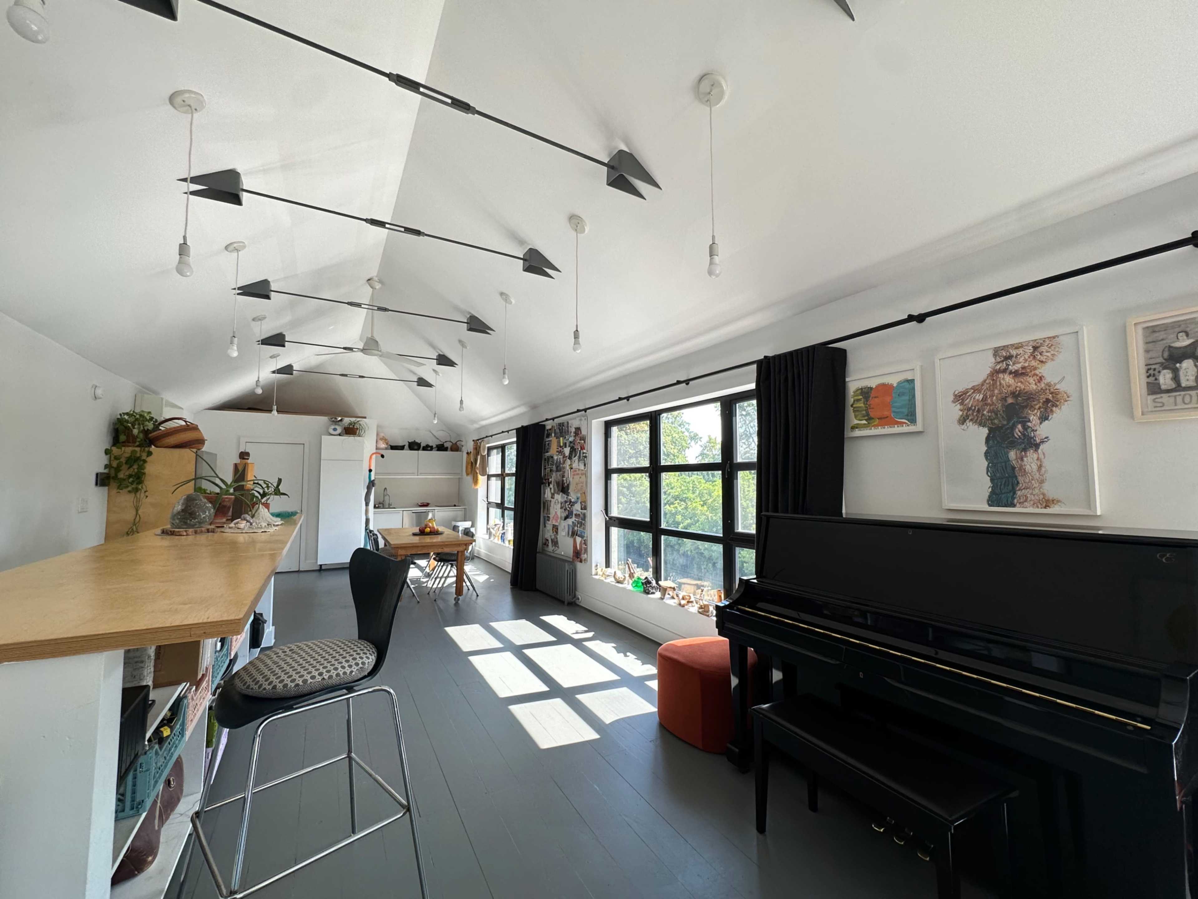 The image shows a bright, modern interior space featuring a piano, bar seating, and large windows that allow natural light to fill the room.