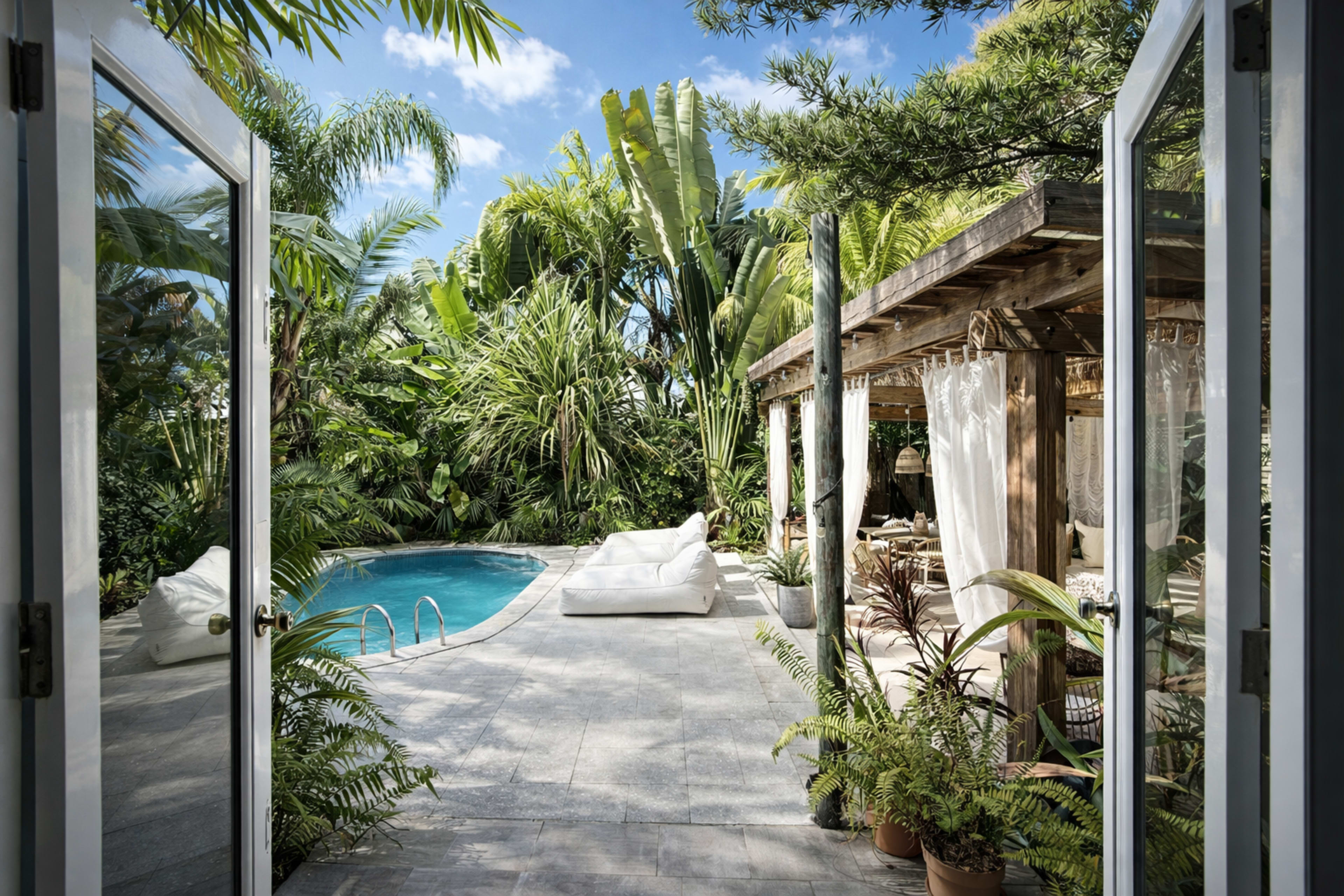 A view from an open doorway reveals a pool surrounded by lush greenery and a wooden structure with seating.