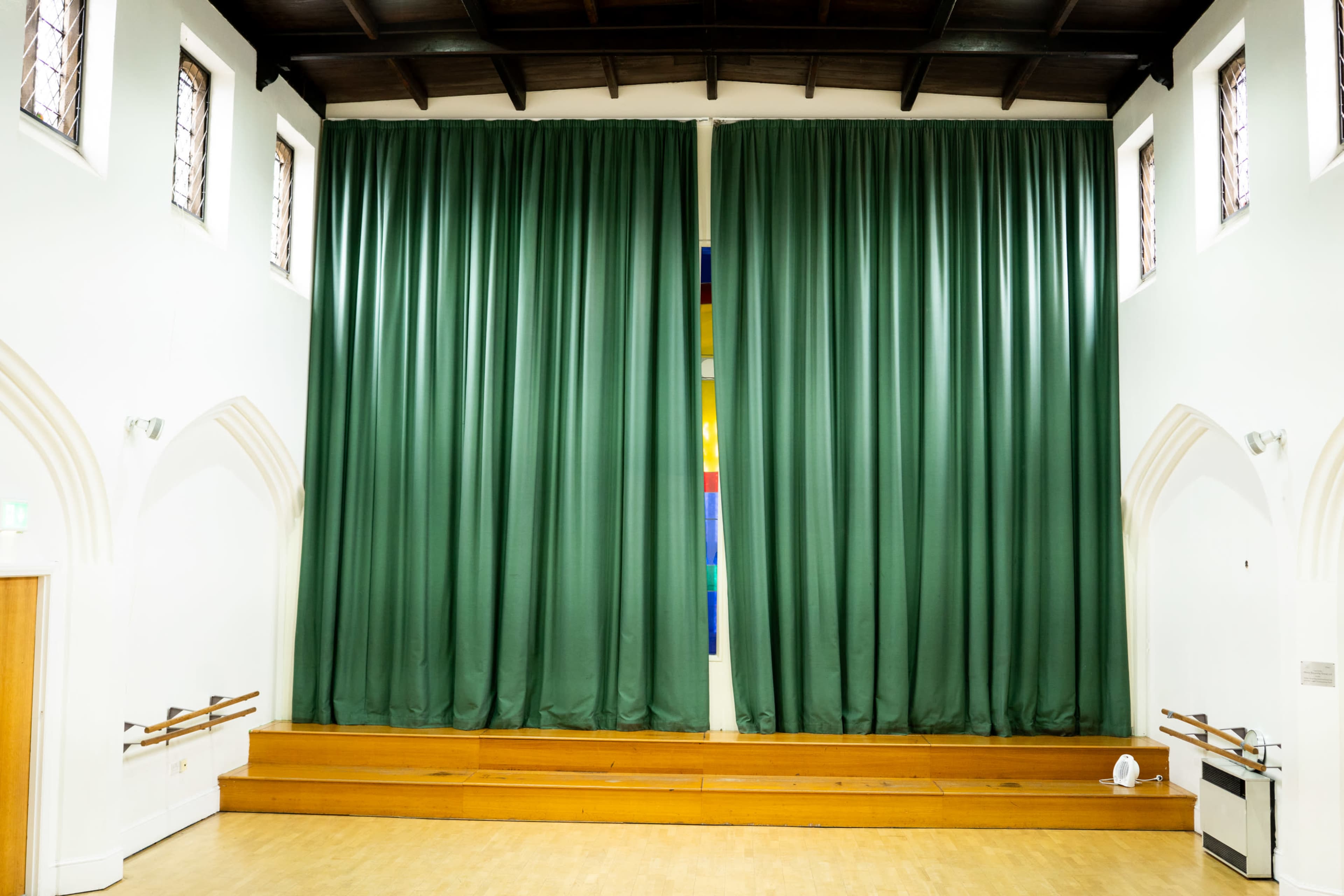 The image shows a stage area in a hall with large green curtains and wooden steps leading up to it.