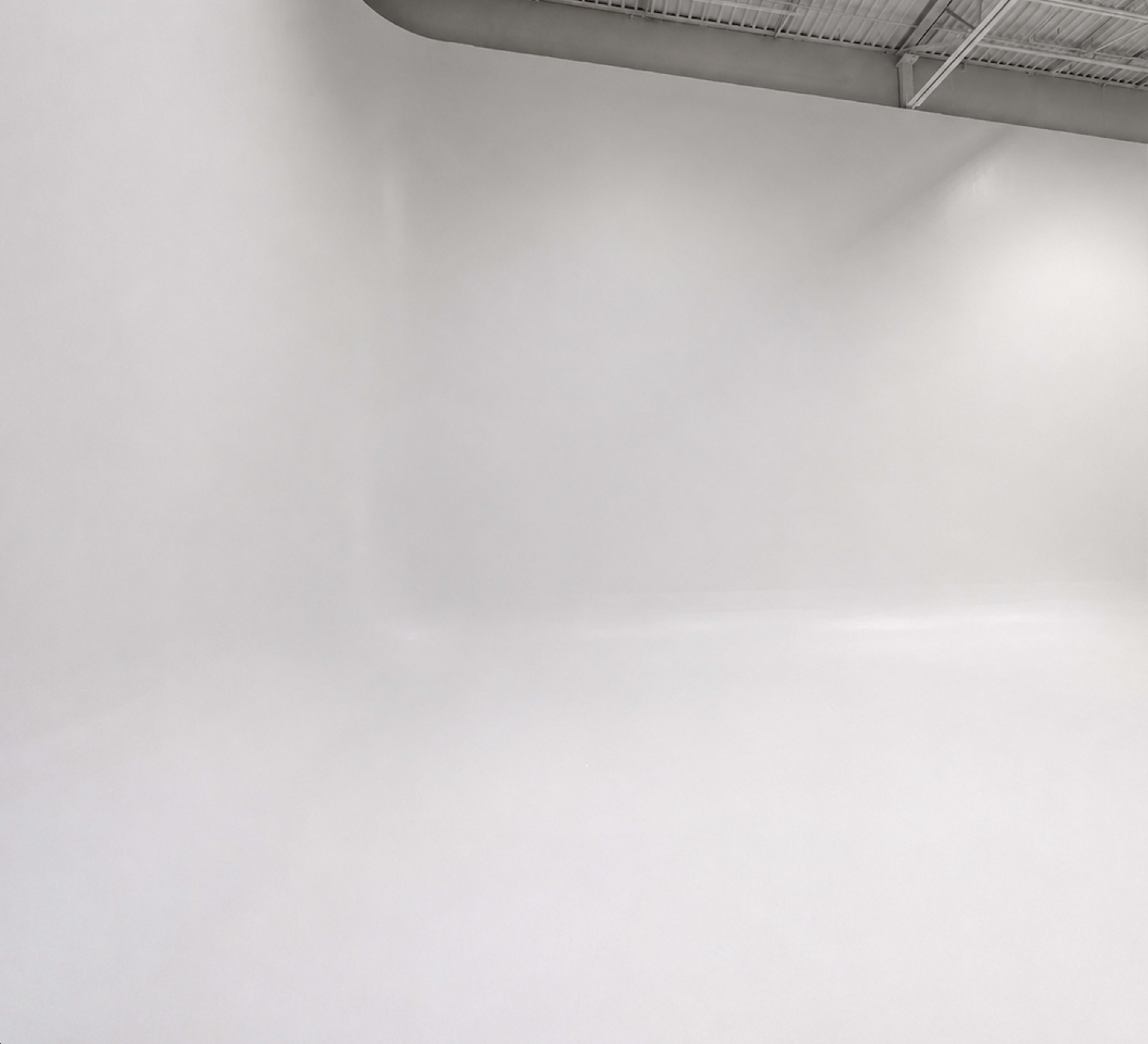 The image shows a spacious, minimally decorated room with white walls and a smooth floor.